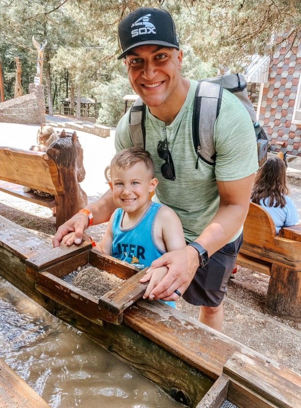 Smiling adult and child at a wooden water flume, outdoors in a forest setting