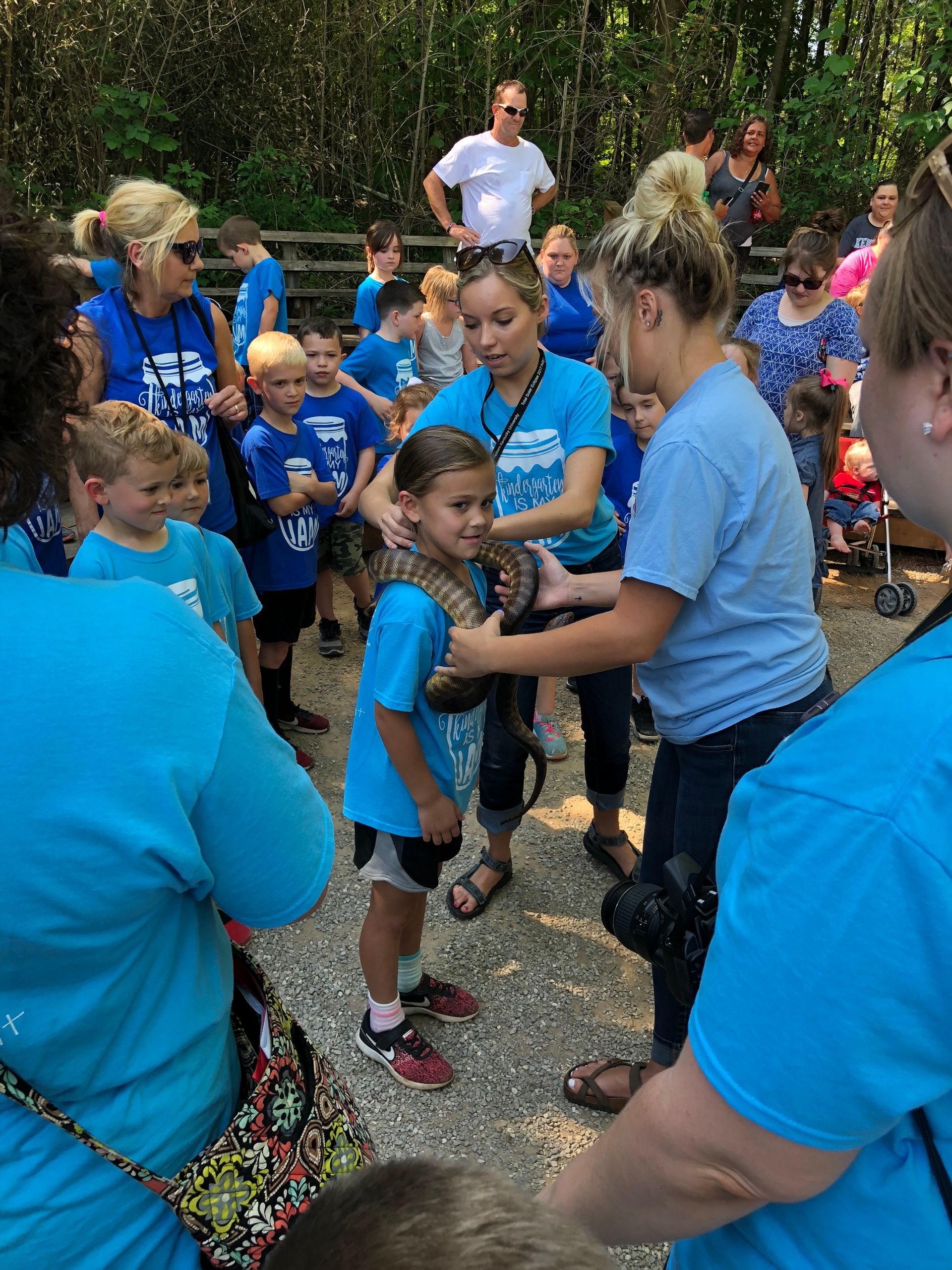 Children in blue shirts playing tug-of-war outdoors while adults supervise nearby