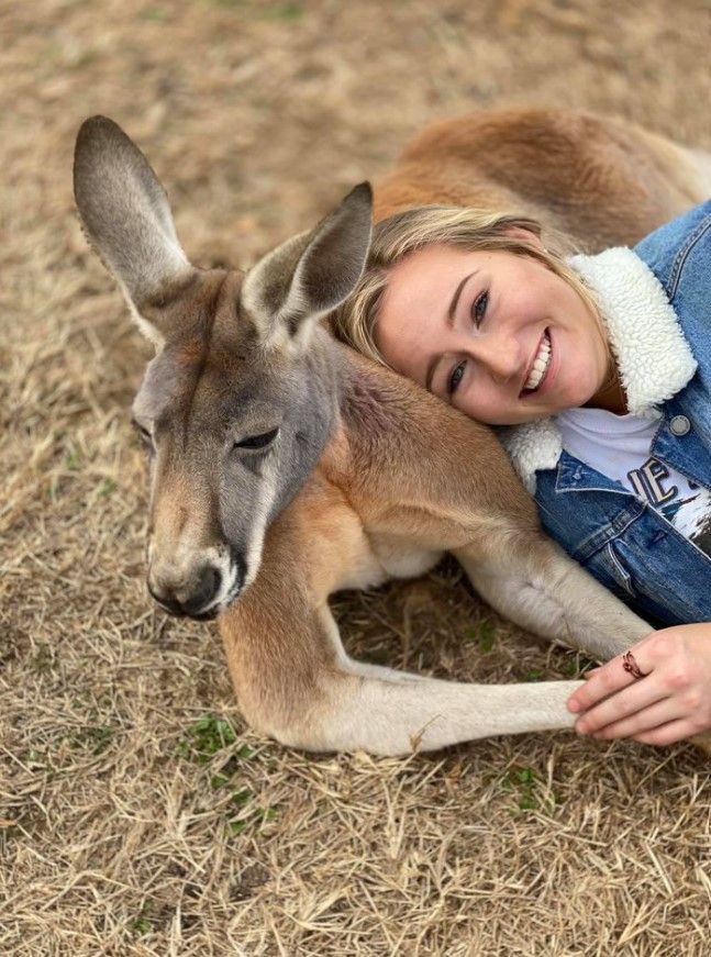 Woman smiling beside resting kangaroo on dry grass