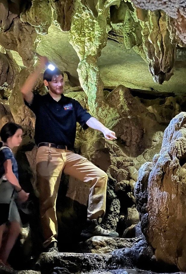 People exploring a rocky cave, one using a headlamp and stepping up on uneven ground