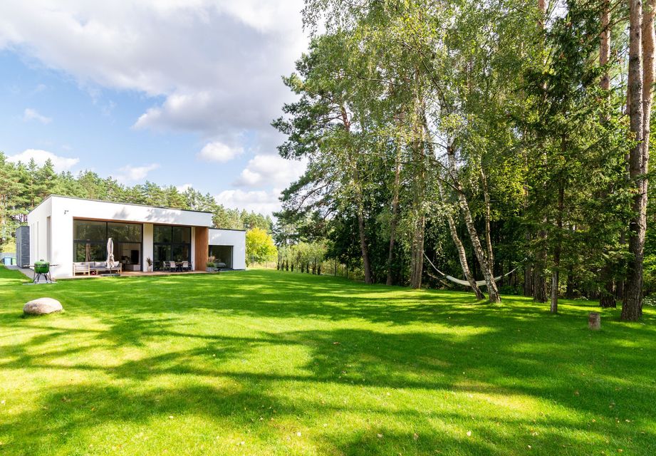 A modern house with a large lawn in front of it surrounded by trees.