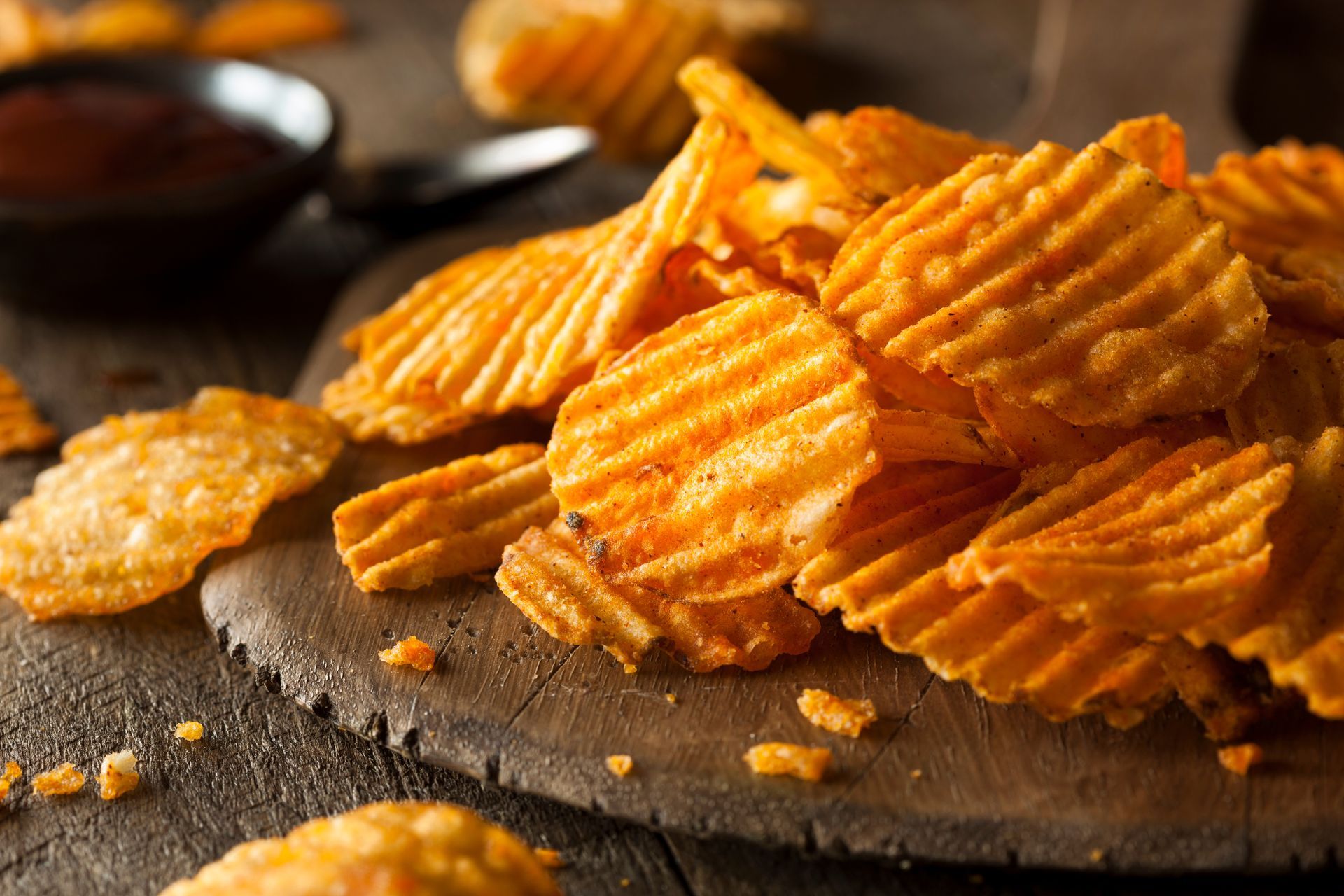A pile of potato chips on a wooden cutting board.