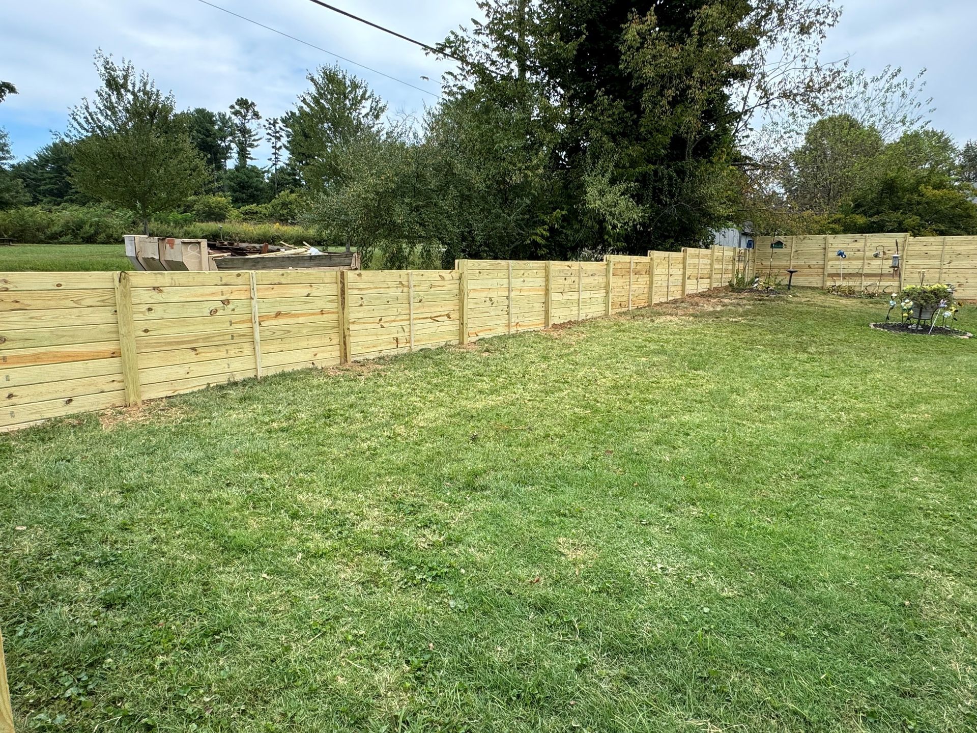 Backyard with a wooden fence, green lawn, and trees under a cloudy sky