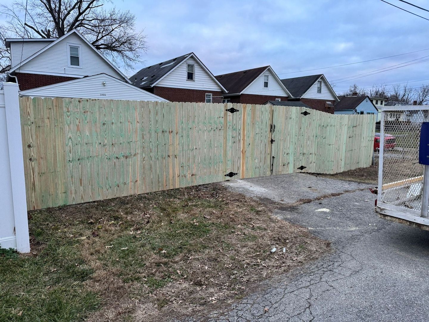 Wooden fence panels blocking a gravel driveway beside houses under a cloudy sky