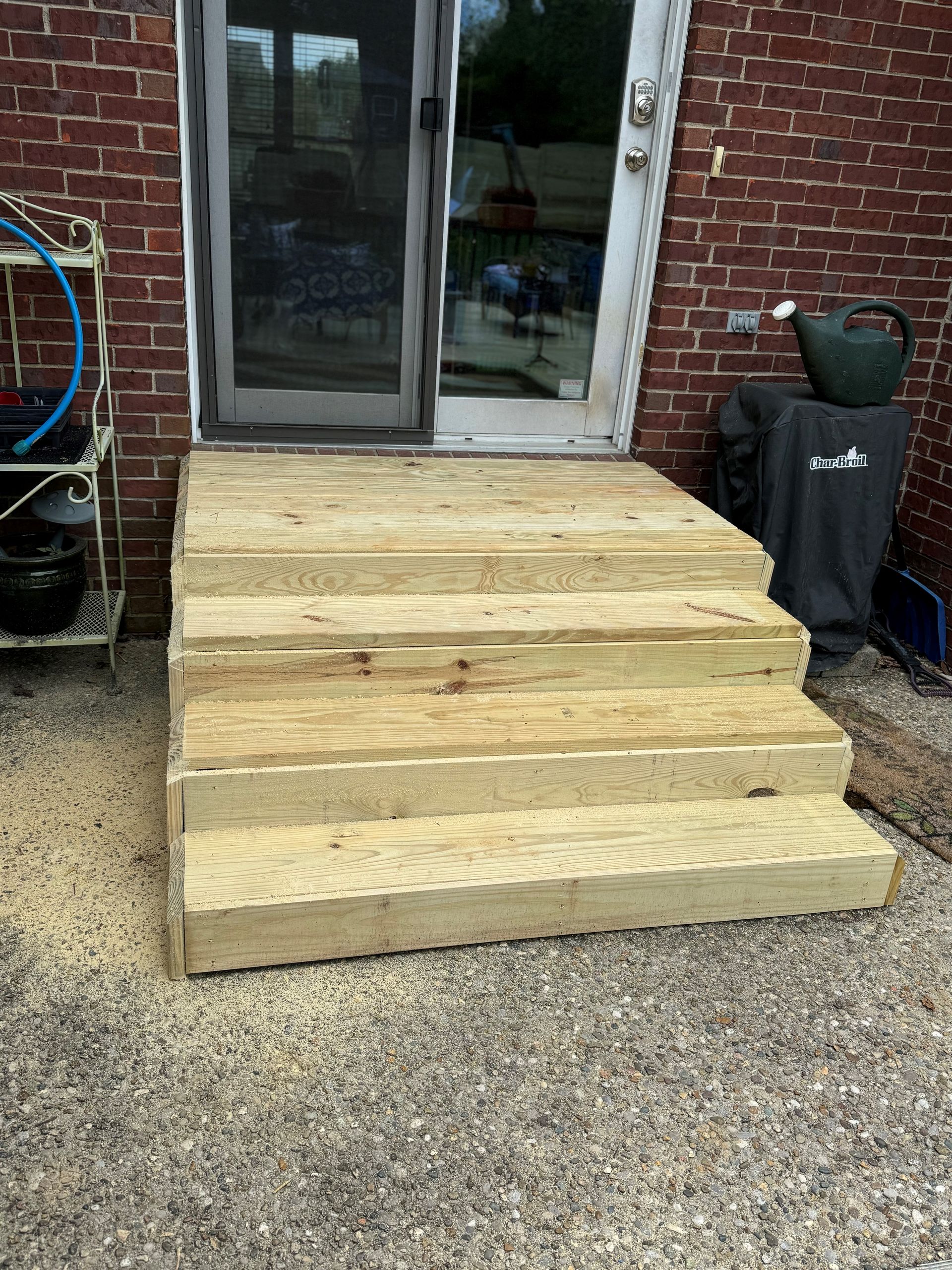 Wooden porch steps leading to a sliding glass door on a brick patio