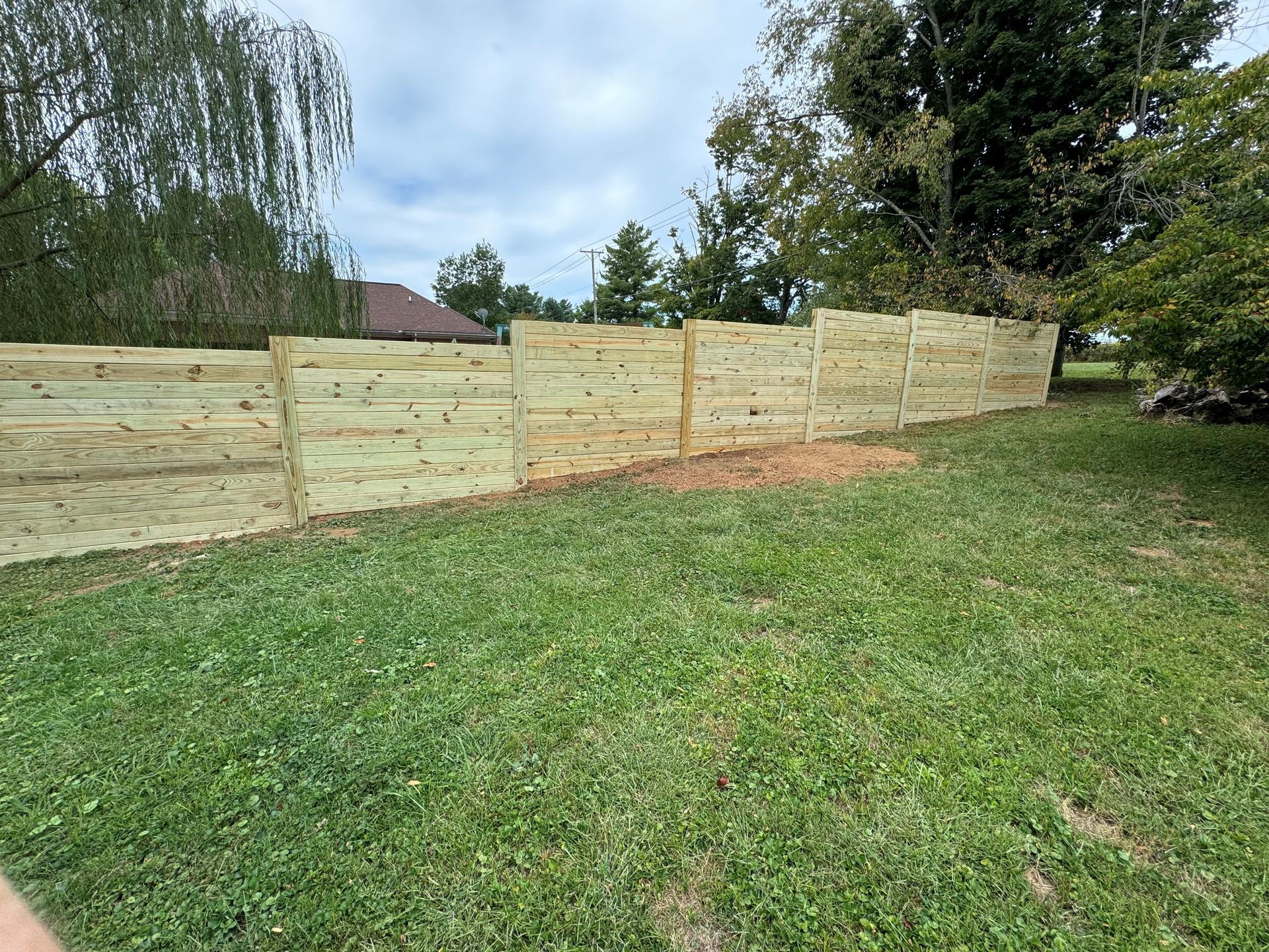 Long wooden fence panels along a grassy yard with trees in the background