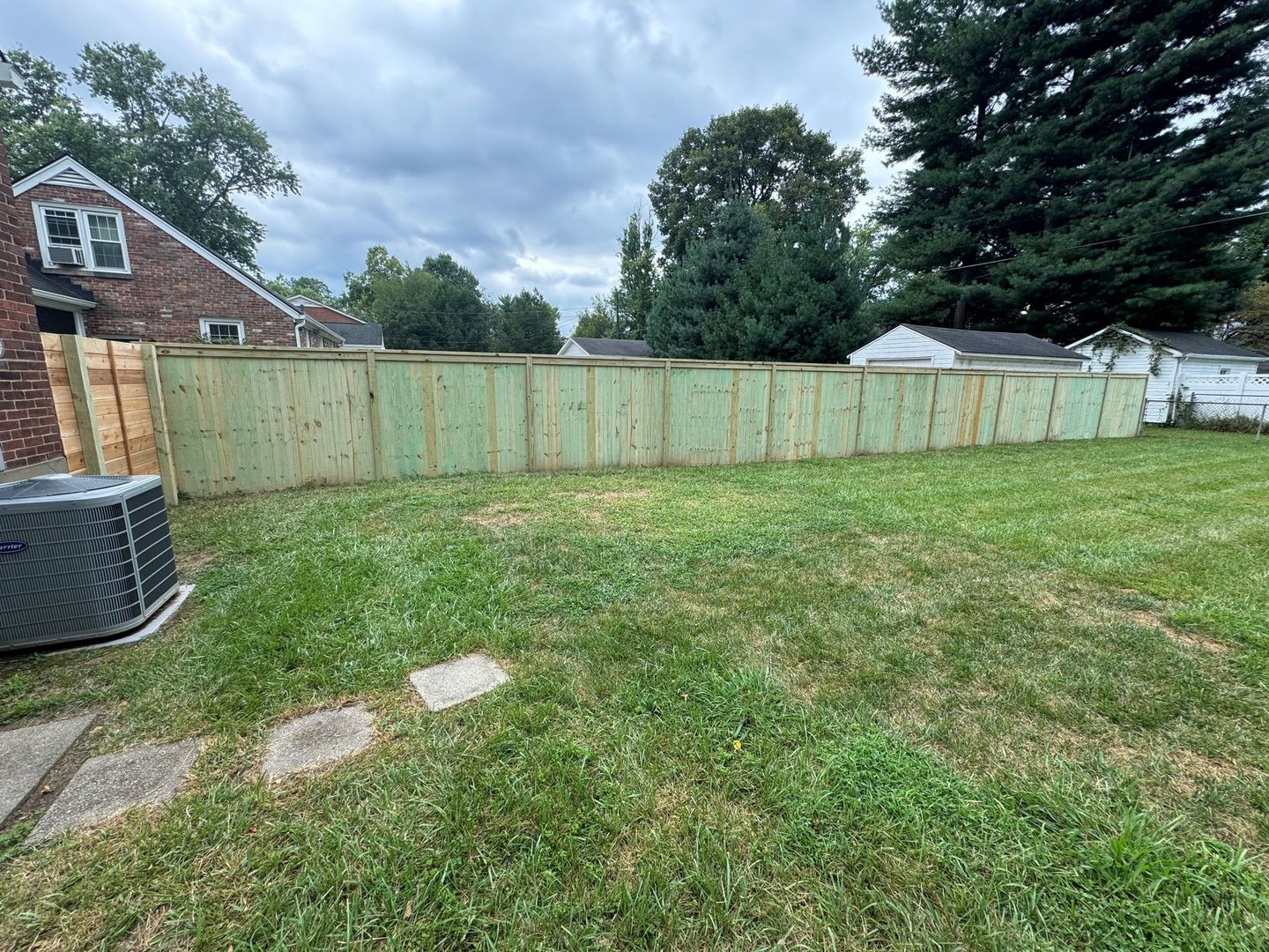 Backyard with a wooden privacy fence, grassy lawn, and cloudy sky