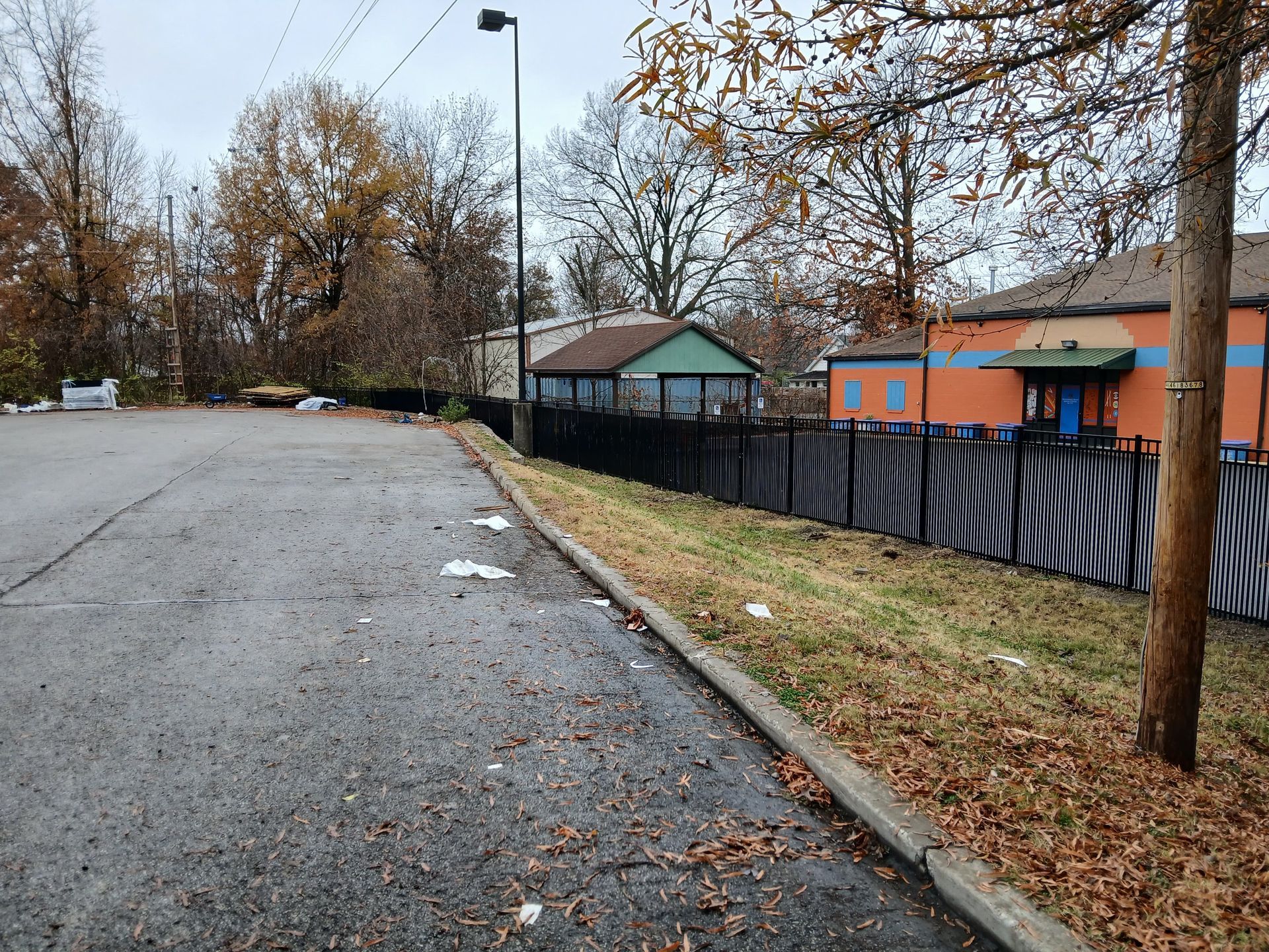 Empty wet parking lot beside a fenced playground with trees and overcast sky