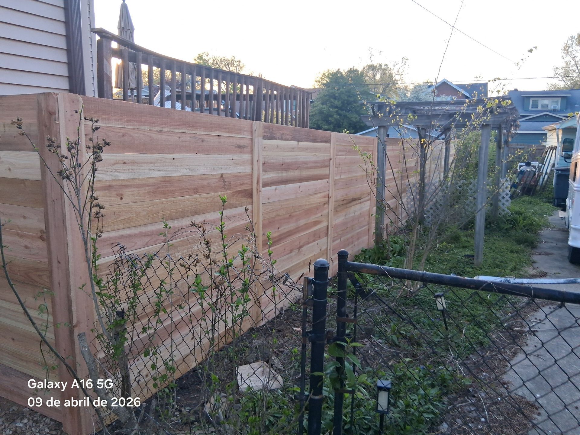 A newly built, horizontal-slat wooden privacy fence stands next to an older chain-link fence in a backyard.