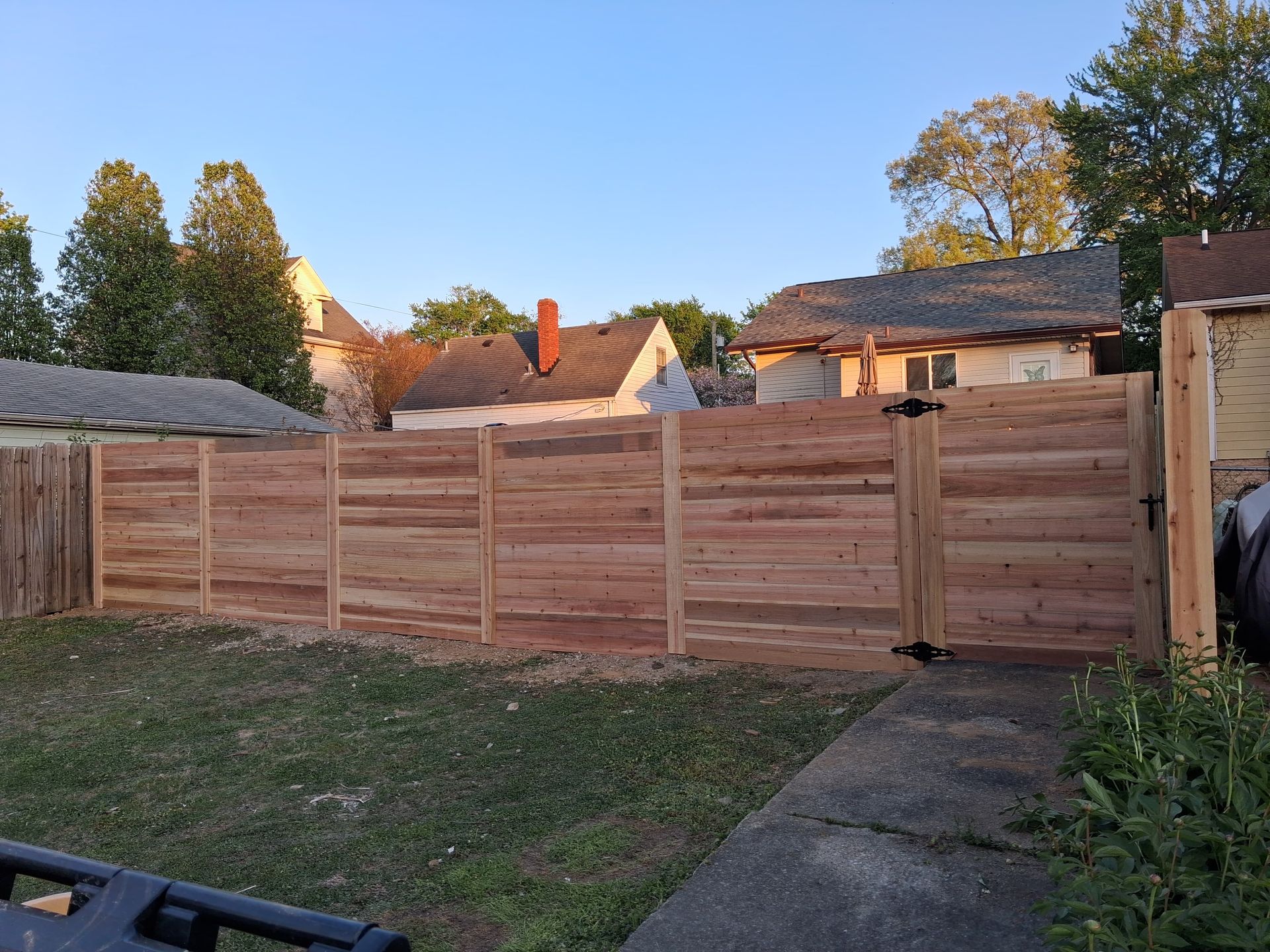 A newly installed wooden horizontal privacy fence spans across a backyard with nearby neighborhood houses in the background.
