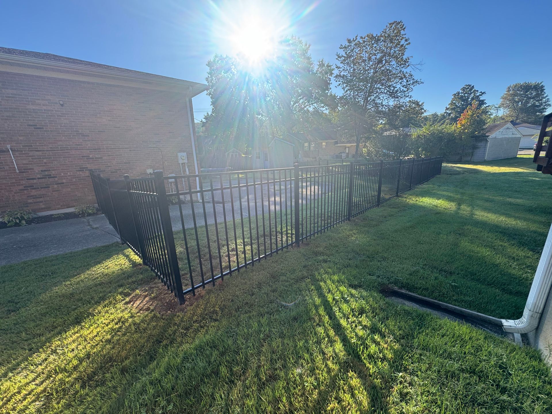 Sunlit backyard fence beside a brick house, with long shadows across the grass.
