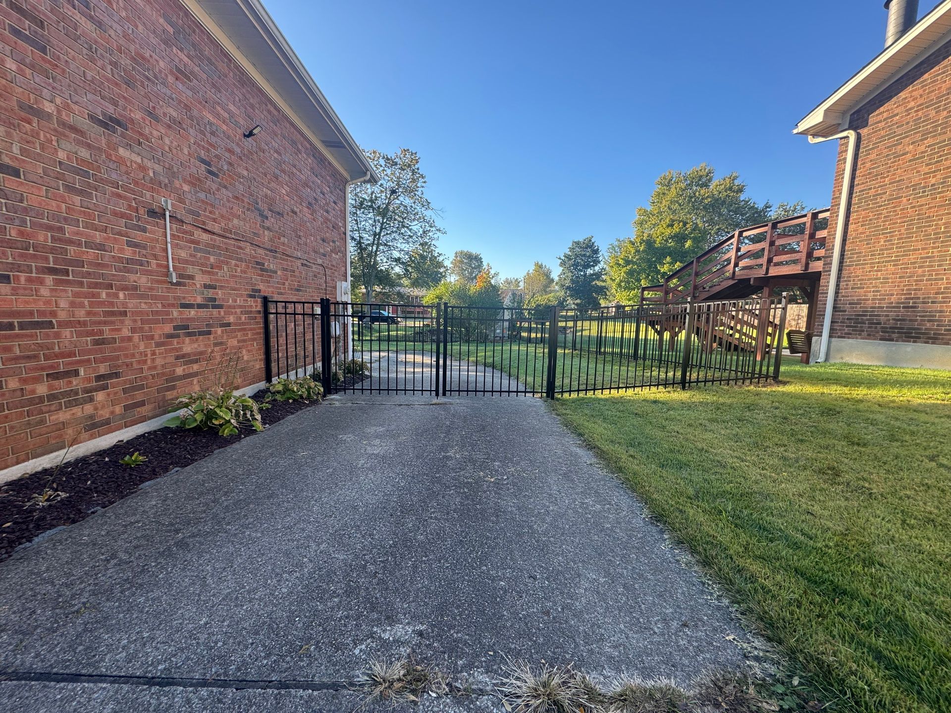Gravel path leading to a black gate between brick apartment buildings and a grassy courtyard