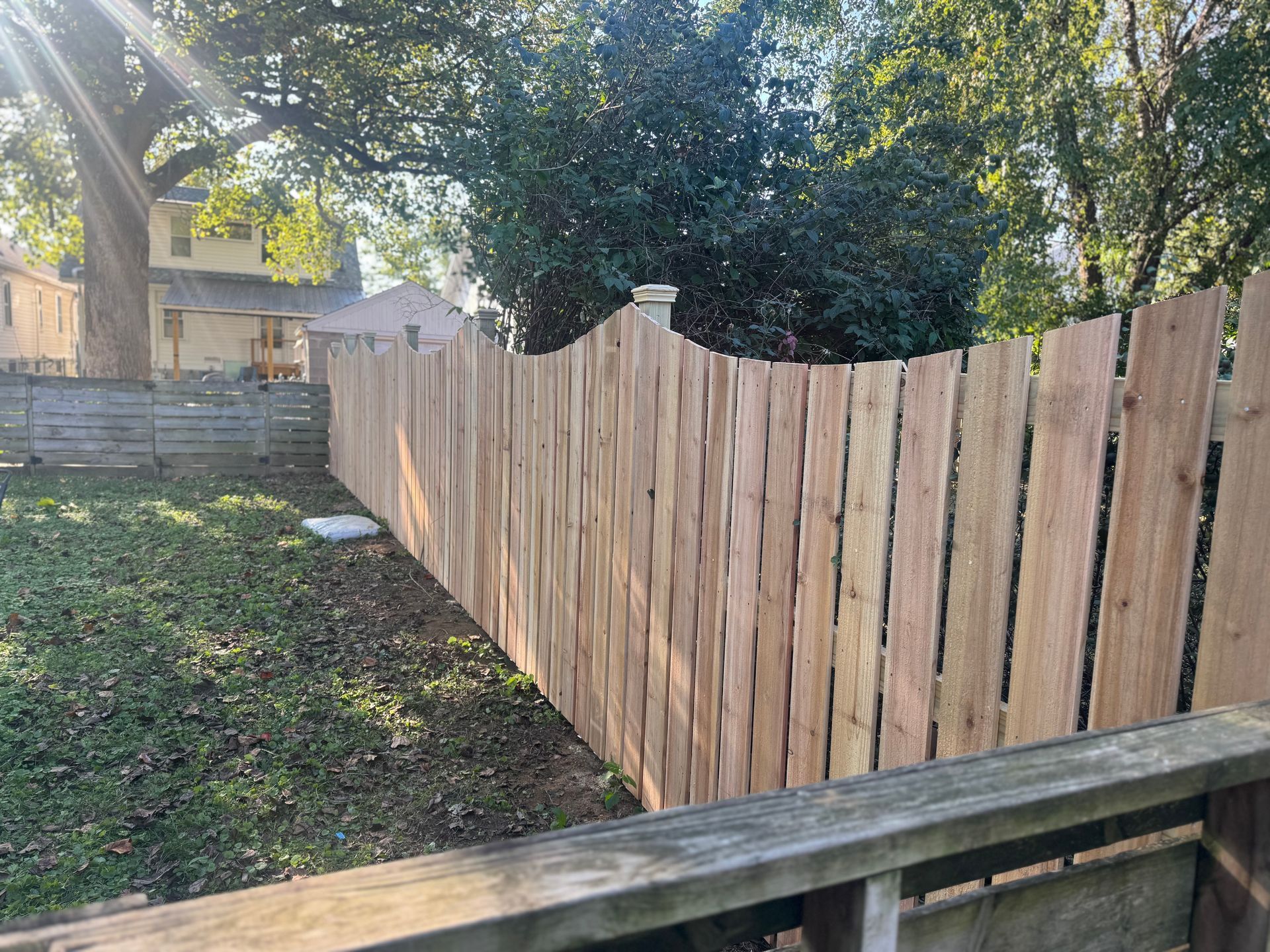 Backyard with a newly built wooden fence beside a grassy yard and house in the background