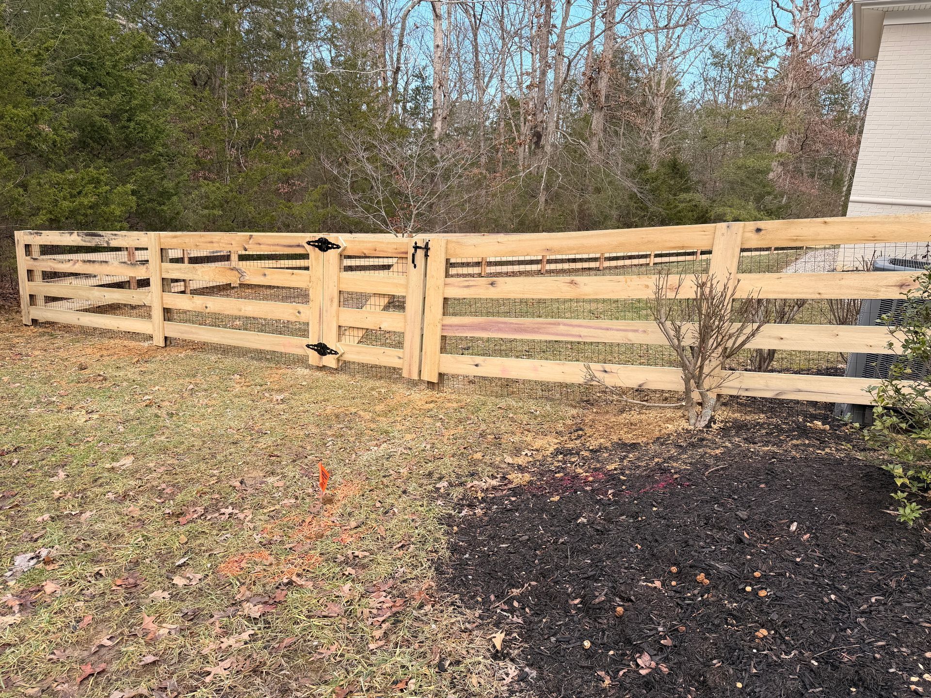 Wooden fence with gate in front yard, brown grass, trees in the background.