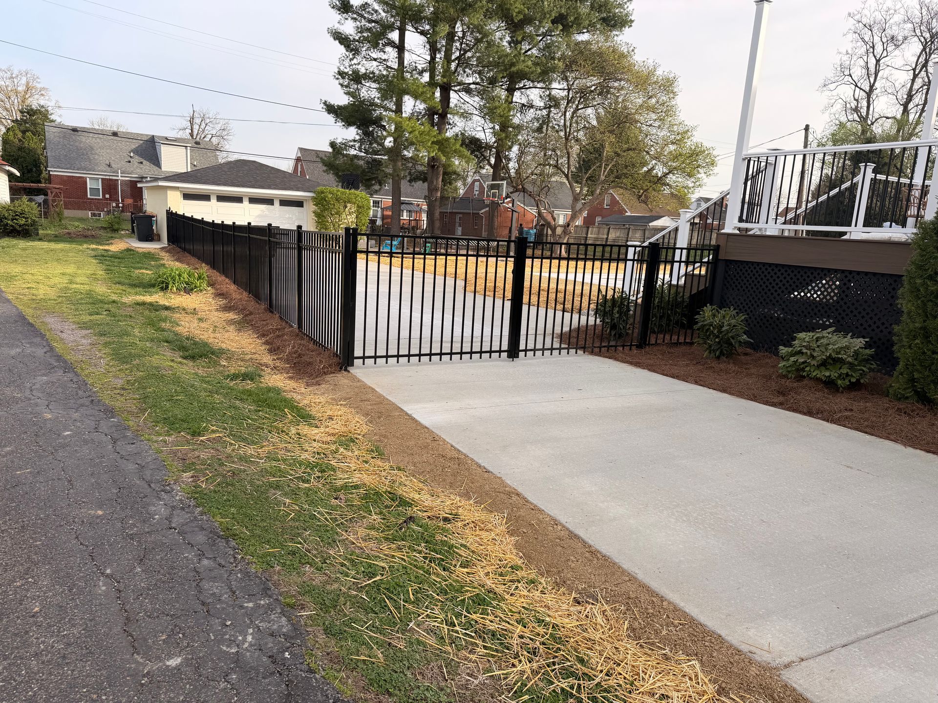 A paved driveway leads to a fenced-in residential backyard with a house and detached garage in the background.
