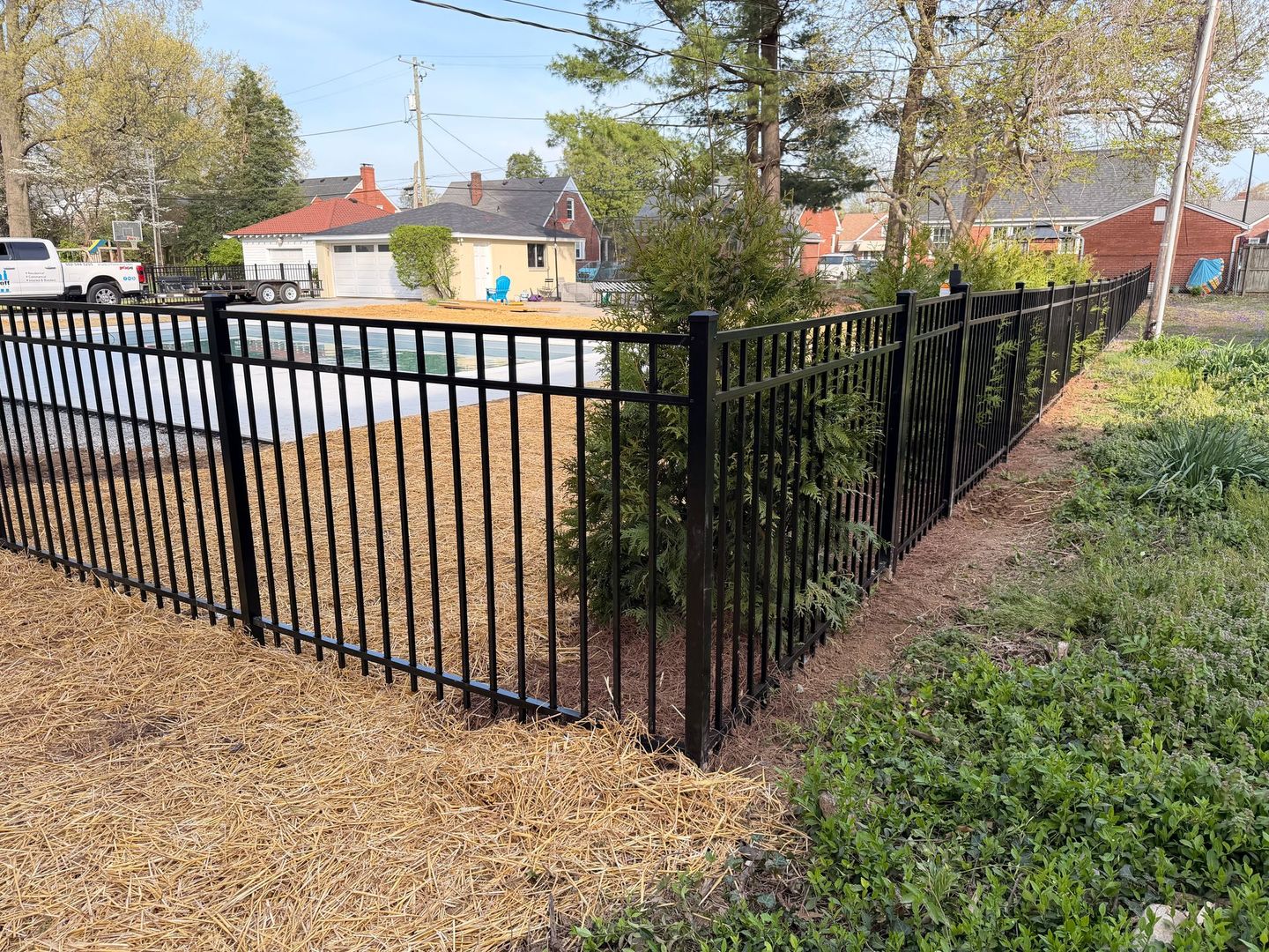 Black metal fence along a gravel path beside a street and grassy area on a sunny day