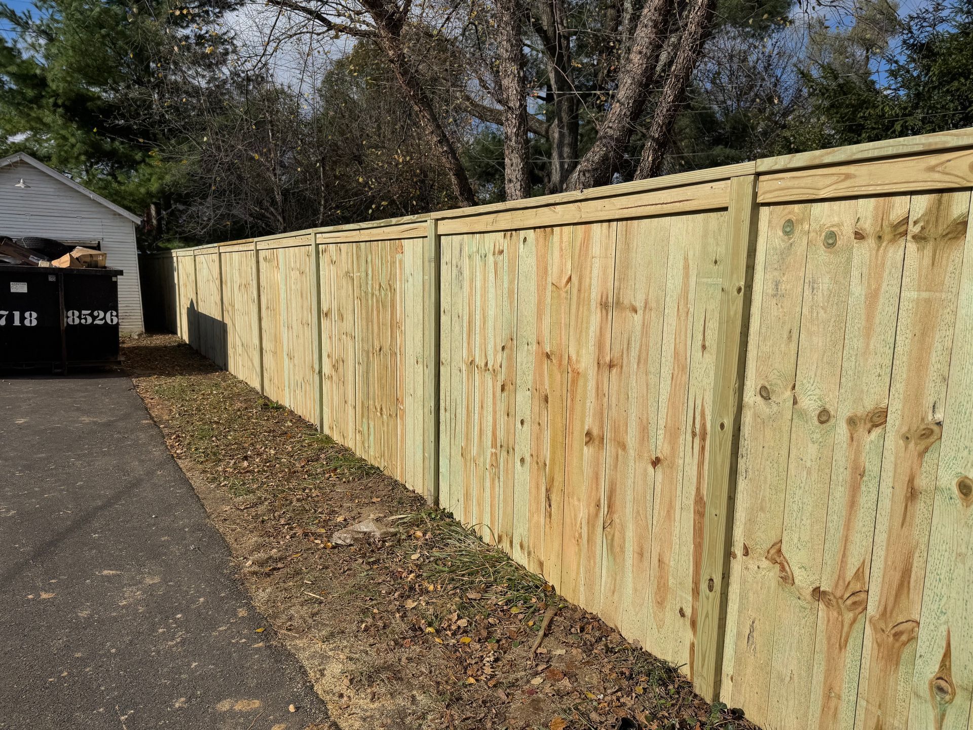 Long wooden privacy fence along a driveway beside a house and garage in daylight