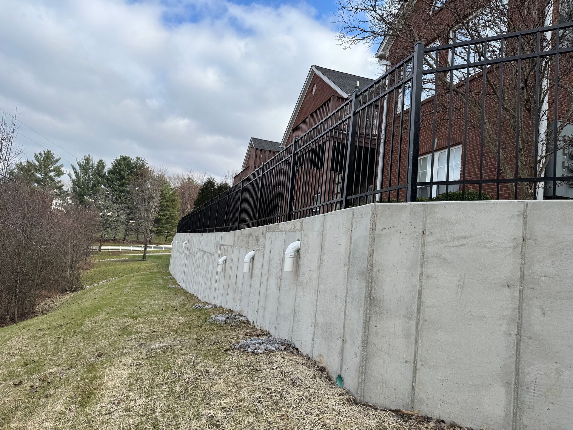 Concrete retaining wall beside grassy path and brick building under cloudy sky