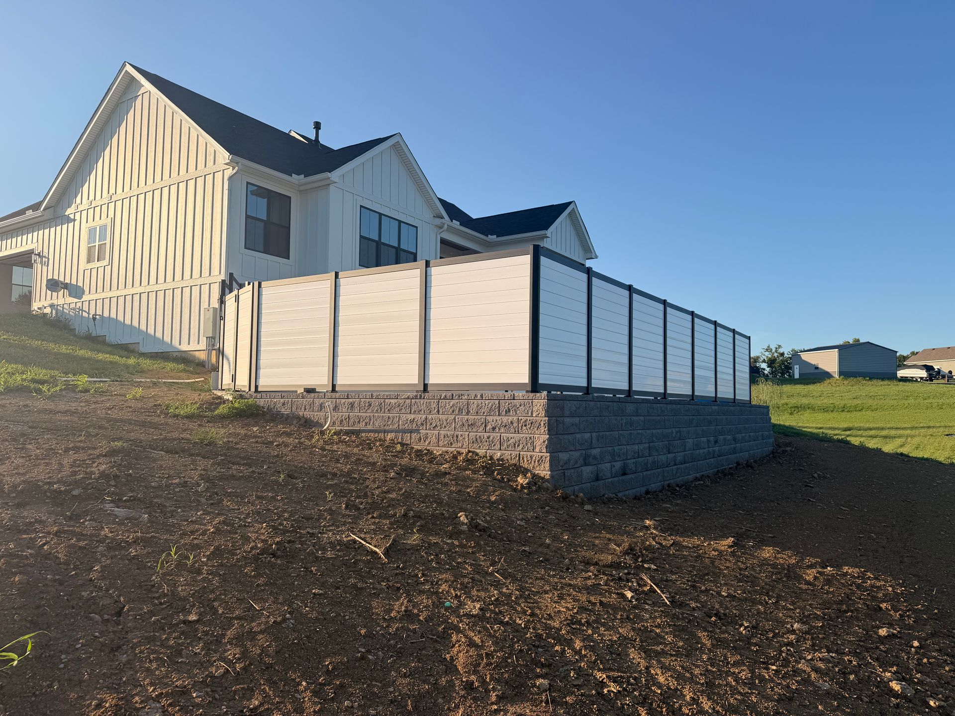 White house with a fenced patio on a grassy hillside under a clear blue sky