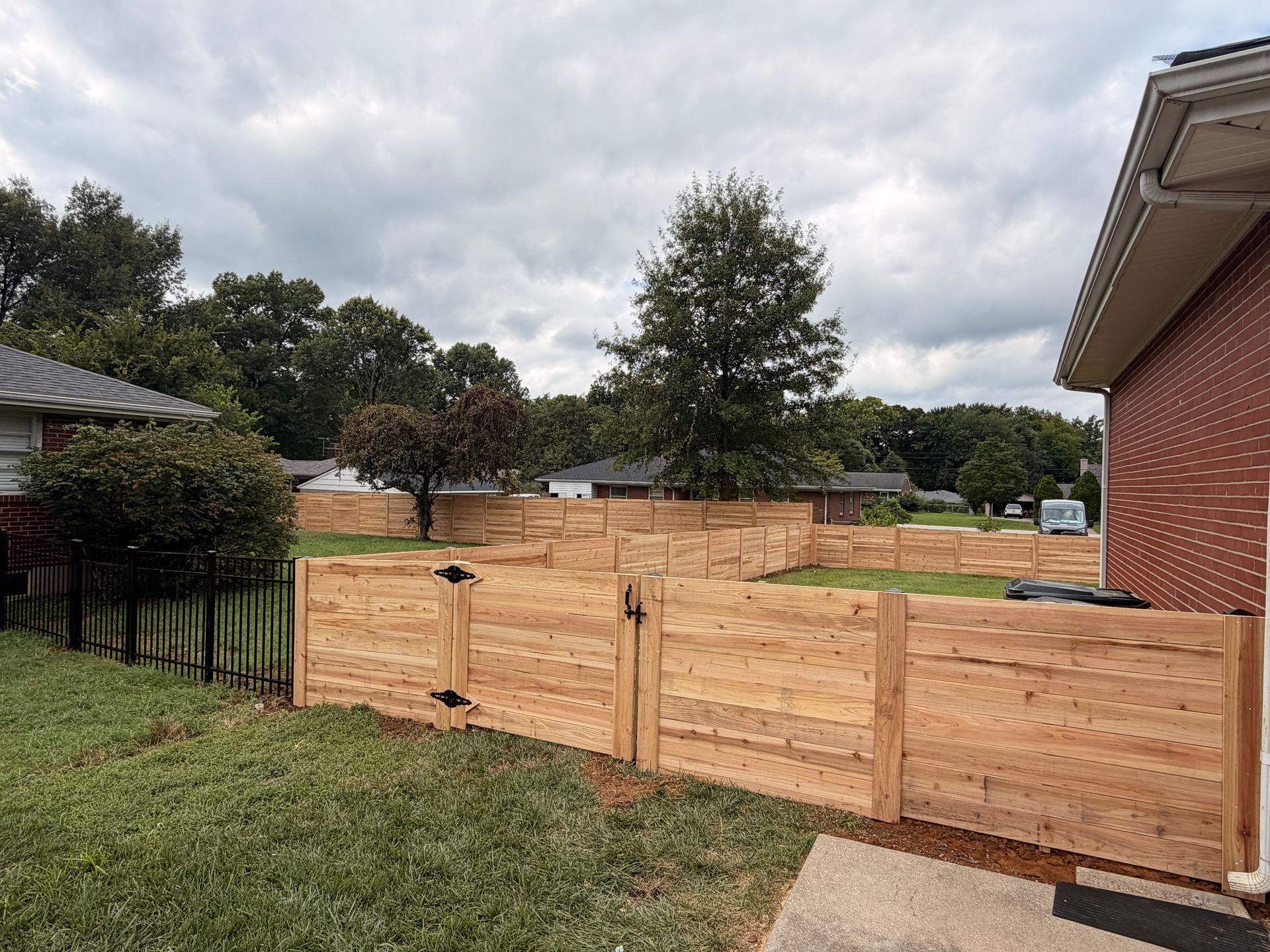 Wooden privacy fence with gate across a grassy yard under a cloudy sky