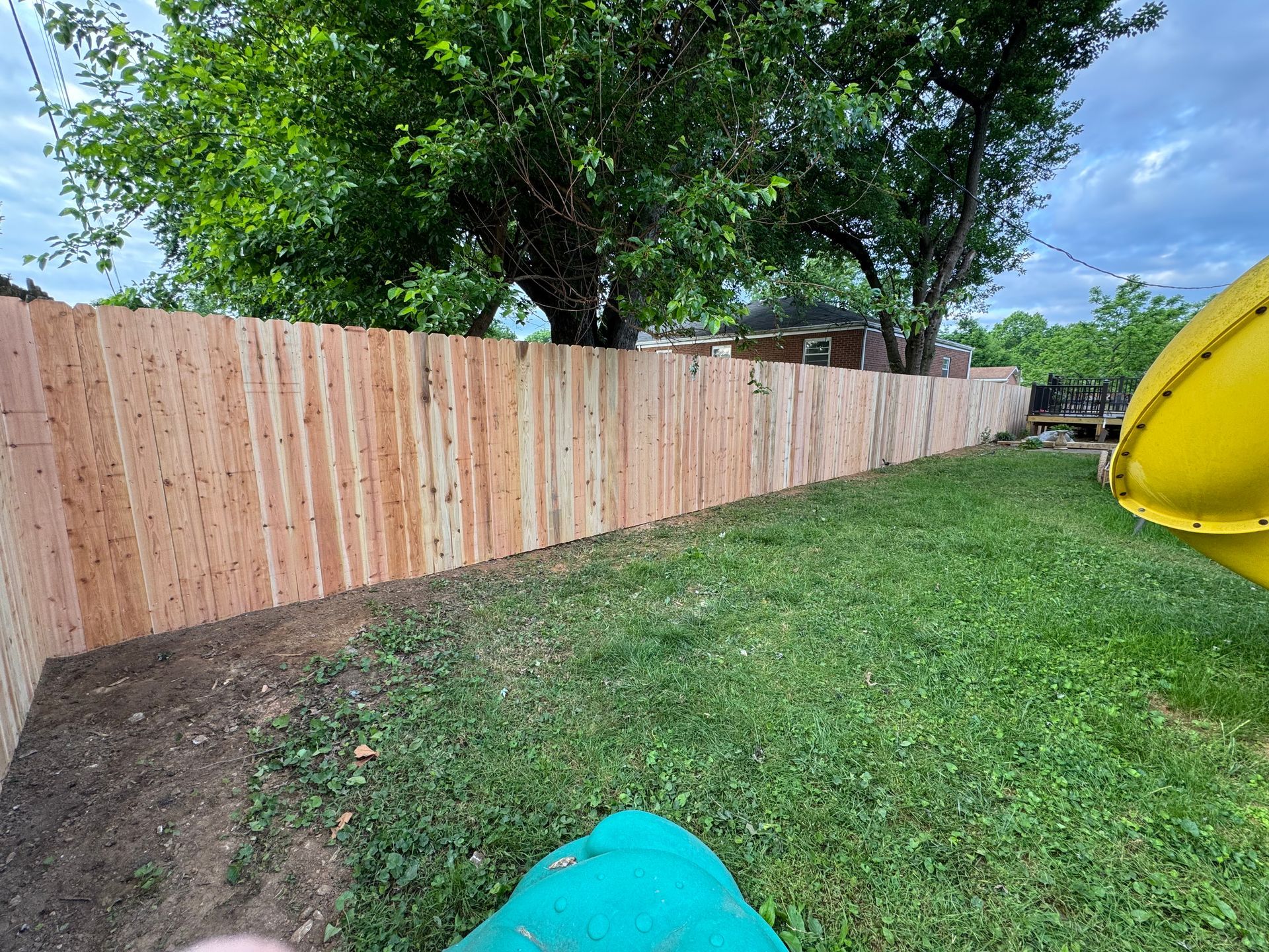 Backyard with wooden fence, green grass, trees, and a yellow slide on the right