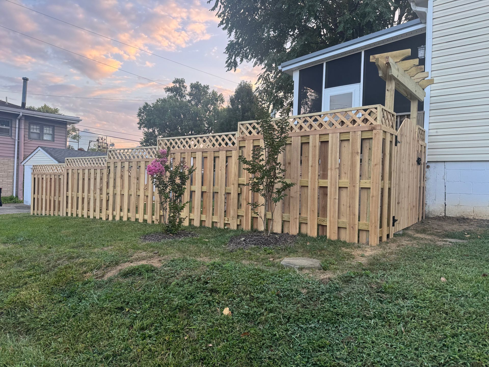 Wooden fenced yard beside a house at sunset, with a small porch and grassy lawn.