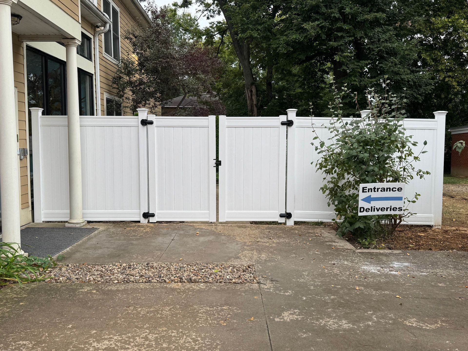 White vinyl fence with gate, entrance sign, and building in the background.