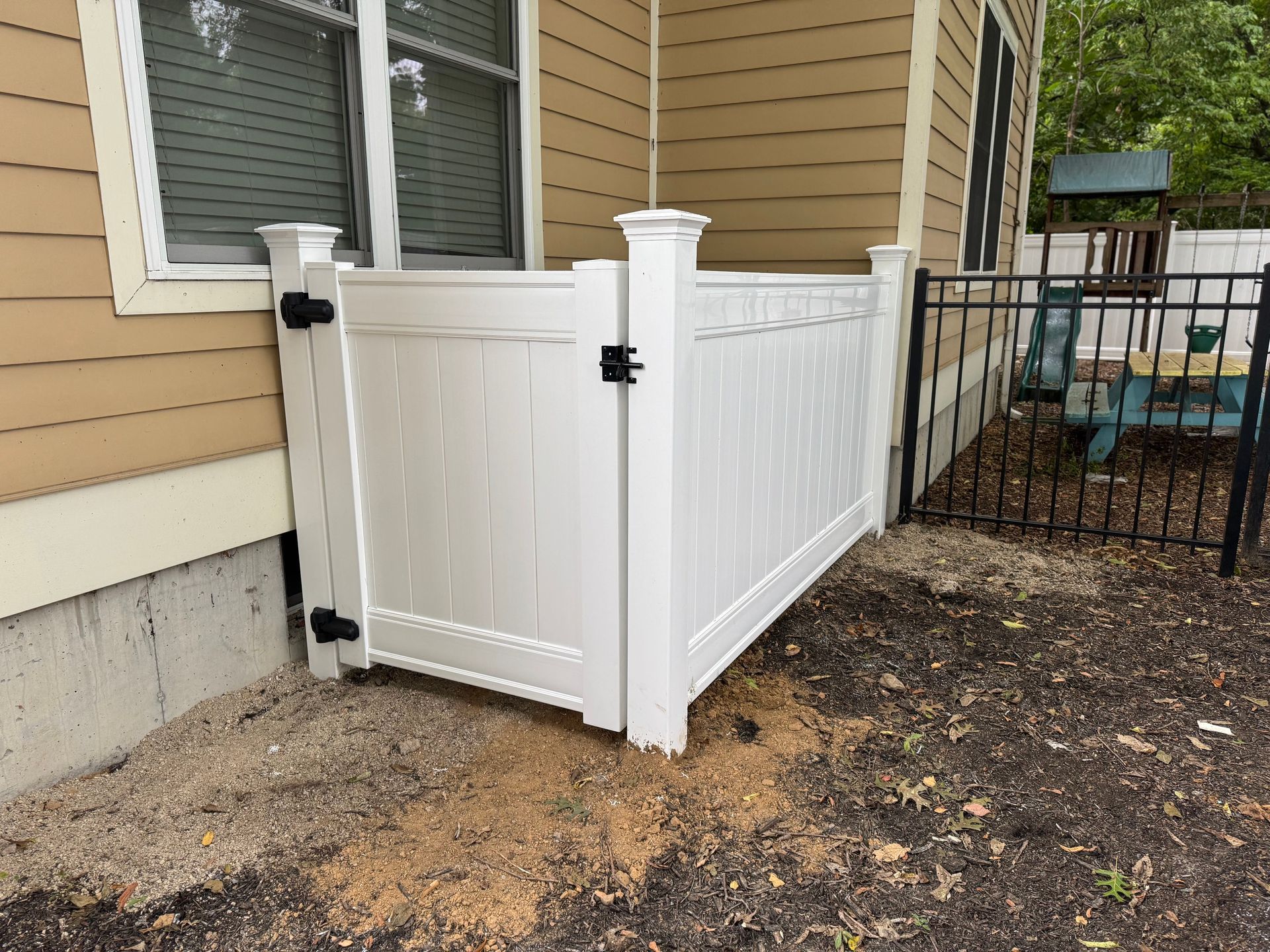 White vinyl privacy fence section with gate, attached to a house.