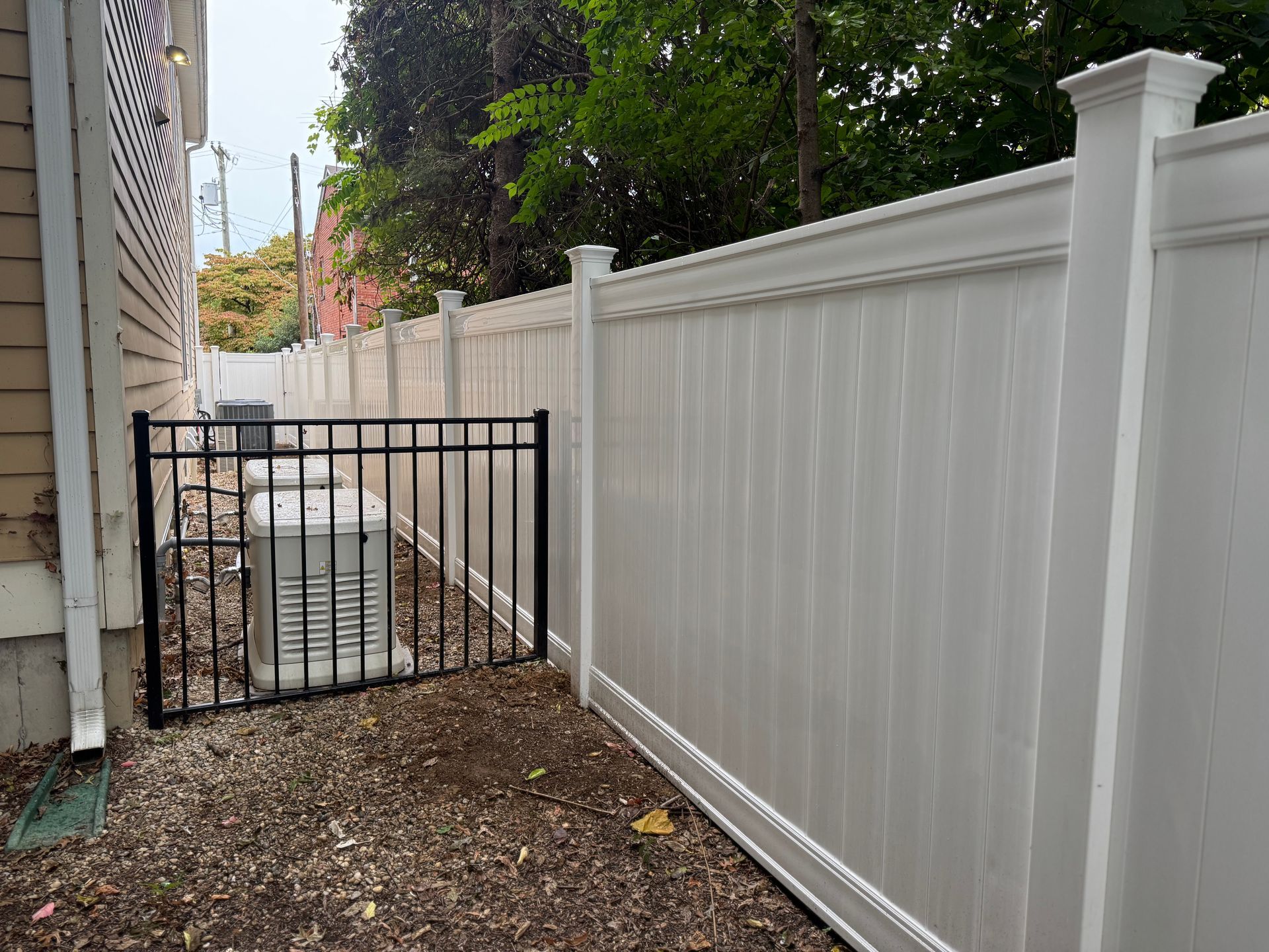 White vinyl fence with black metal gate surrounding a utility unit next to a building.