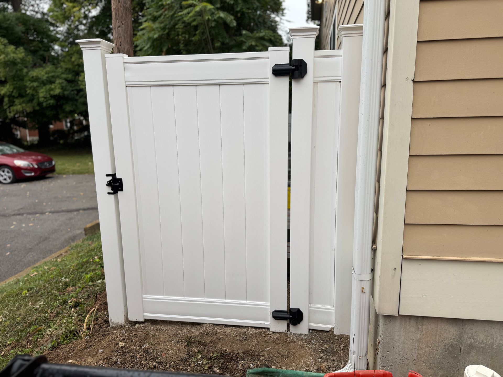 White vinyl gate secured with black latches, next to a beige house, near a street.