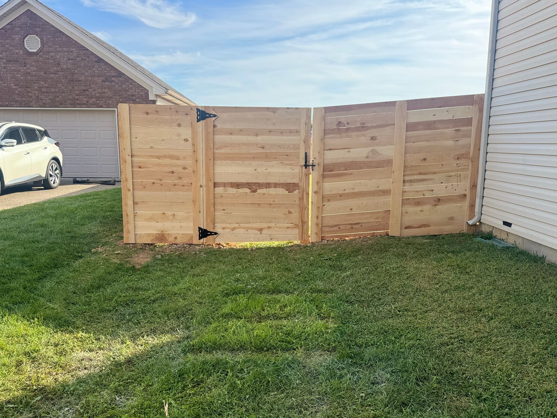 Wooden privacy fence panels in a grassy backyard beside a house, with neighboring homes visible.