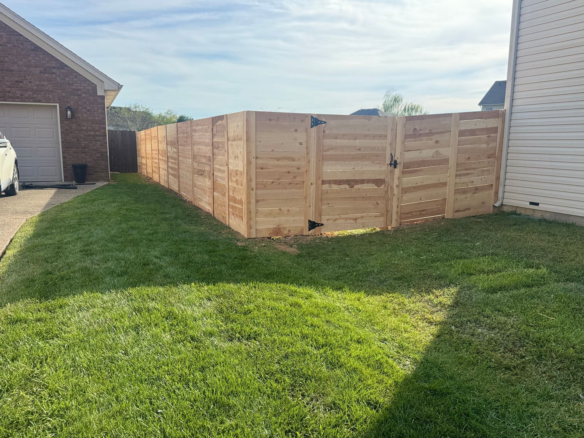 Wooden privacy fence around a backyard corner beside two houses and a green lawn