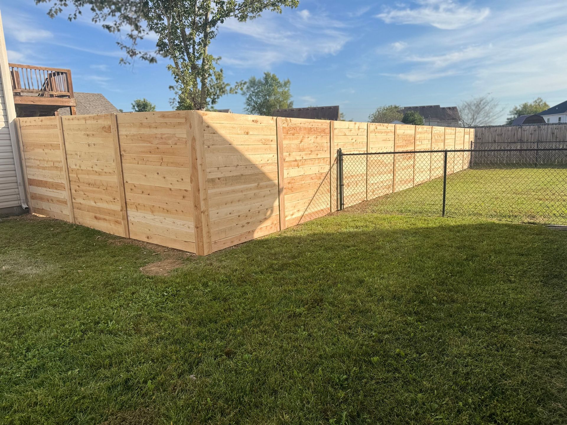 Wooden privacy fence under construction in a grassy backyard on a sunny day