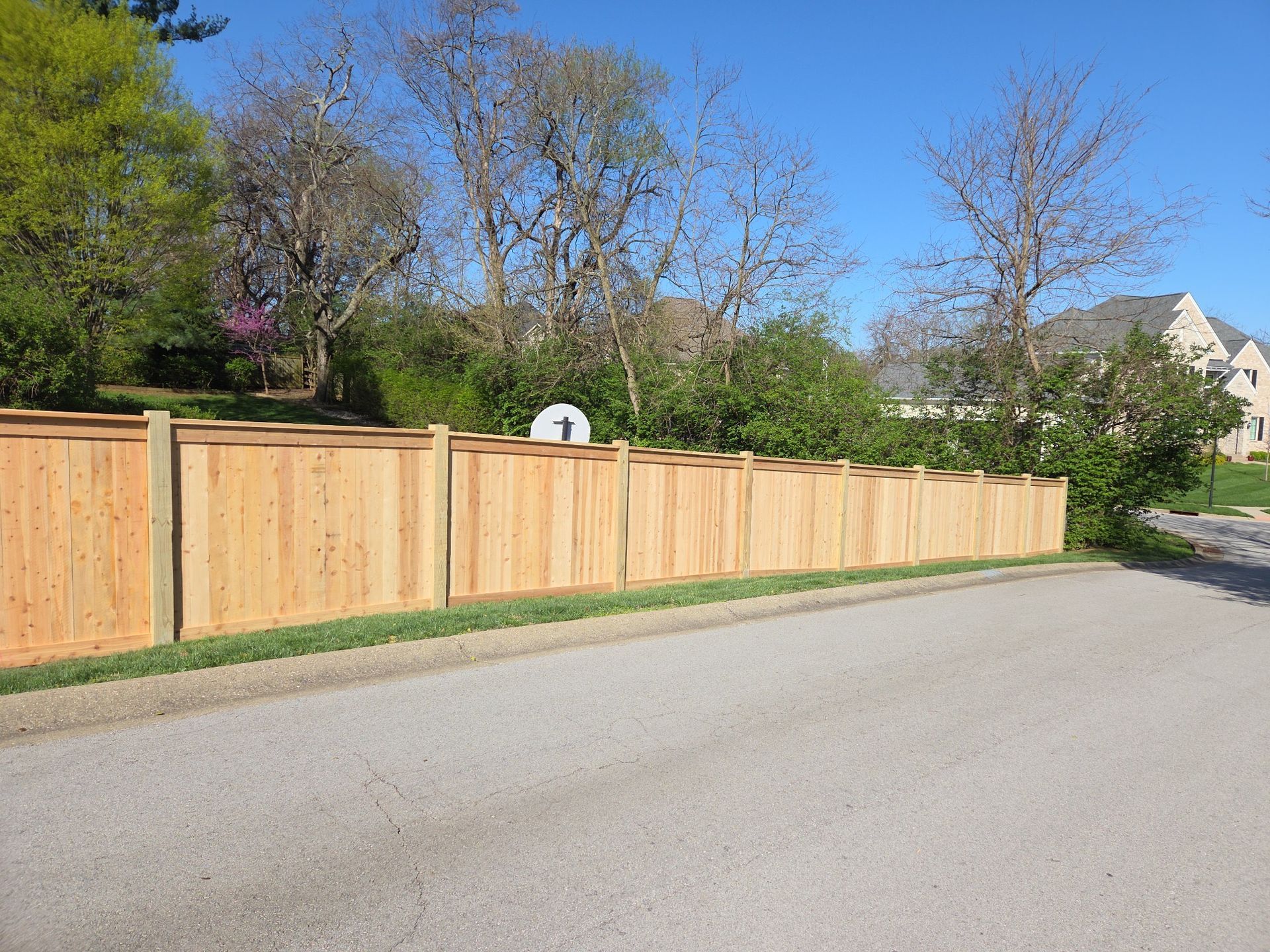 Long wooden privacy fence along a quiet suburban street under a clear blue sky.