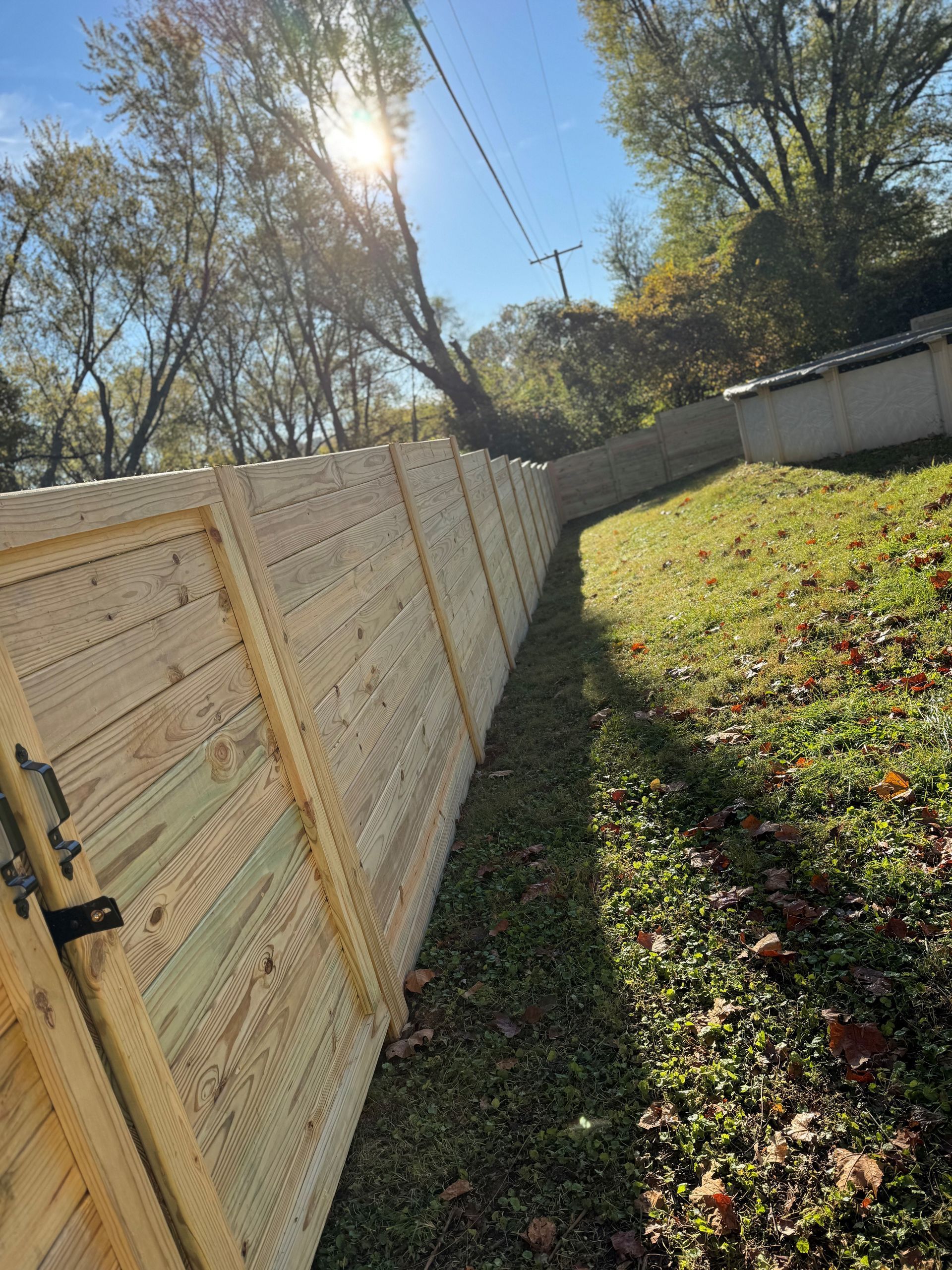 Tilted view of a wooden fence beside a grassy yard under bright sunlight and trees