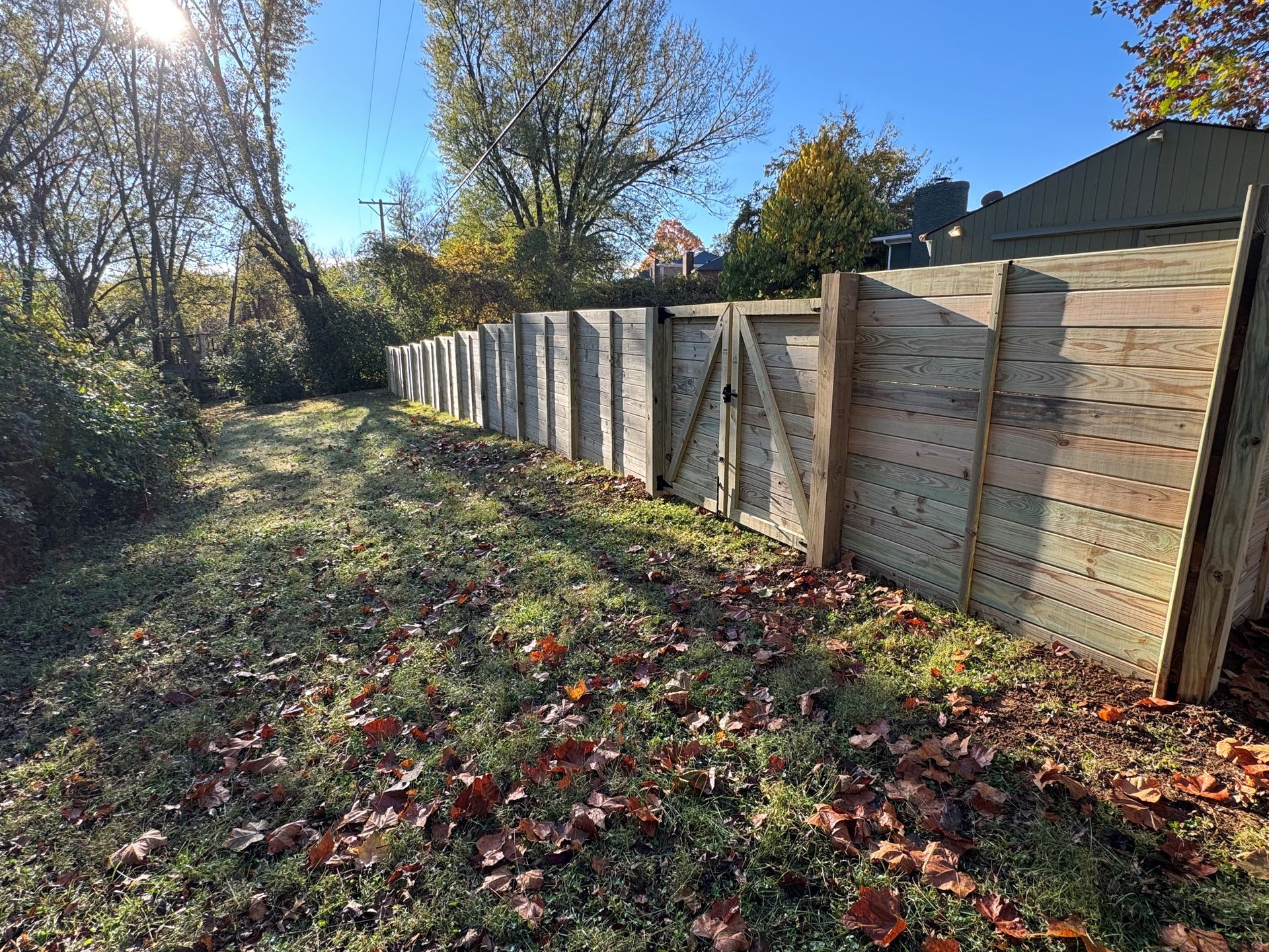 Long wooden fence along a grassy path beside trees on a sunny autumn day