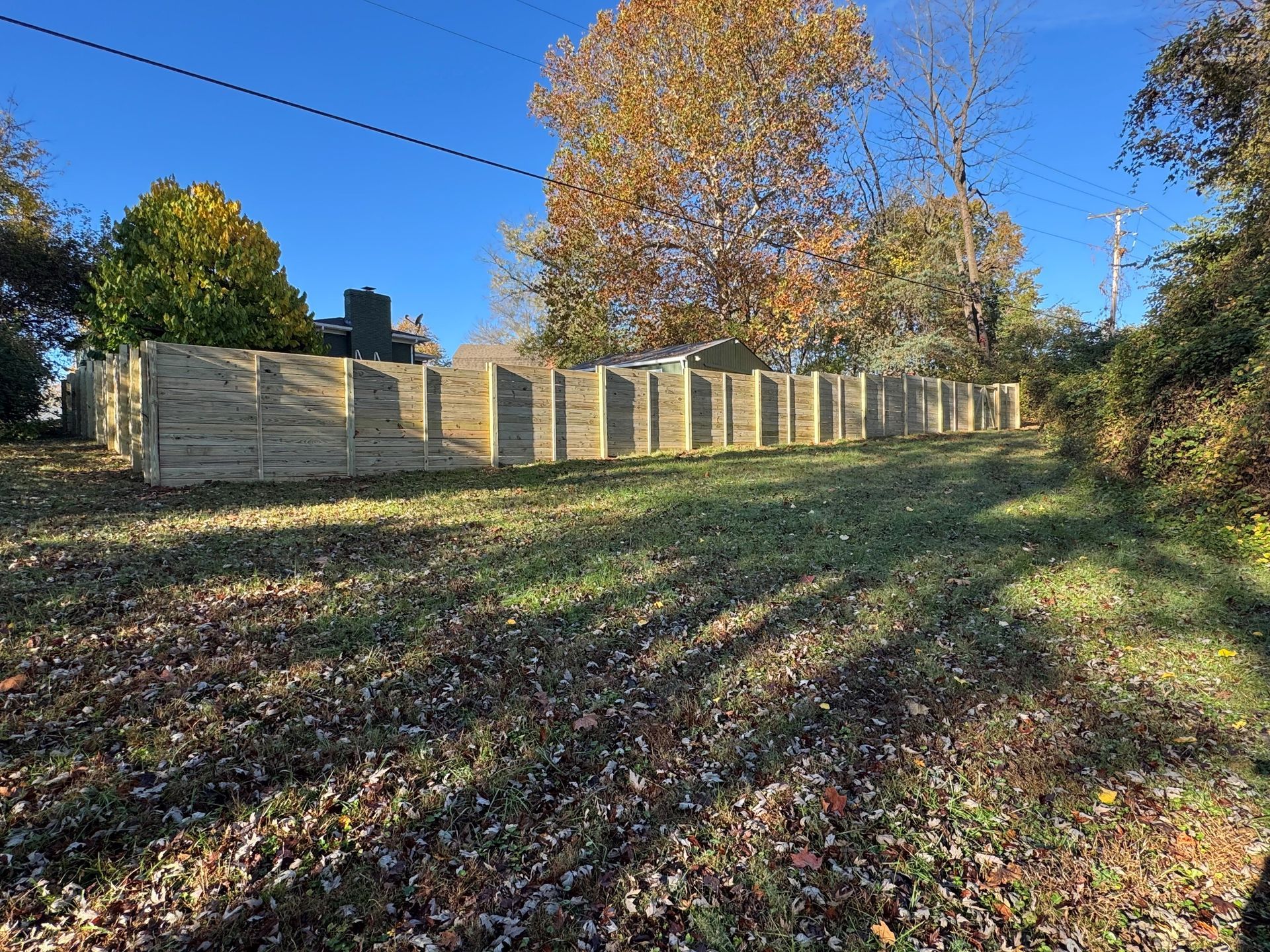 Stone fence along a grassy hillside with autumn trees under a clear blue sky