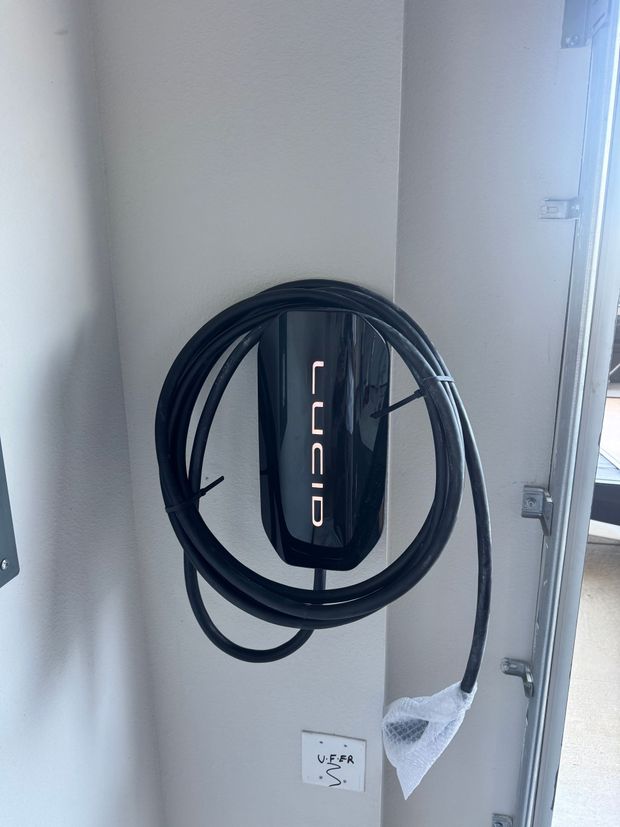 Electric vehicle charger next to electrical panel inside a garage.