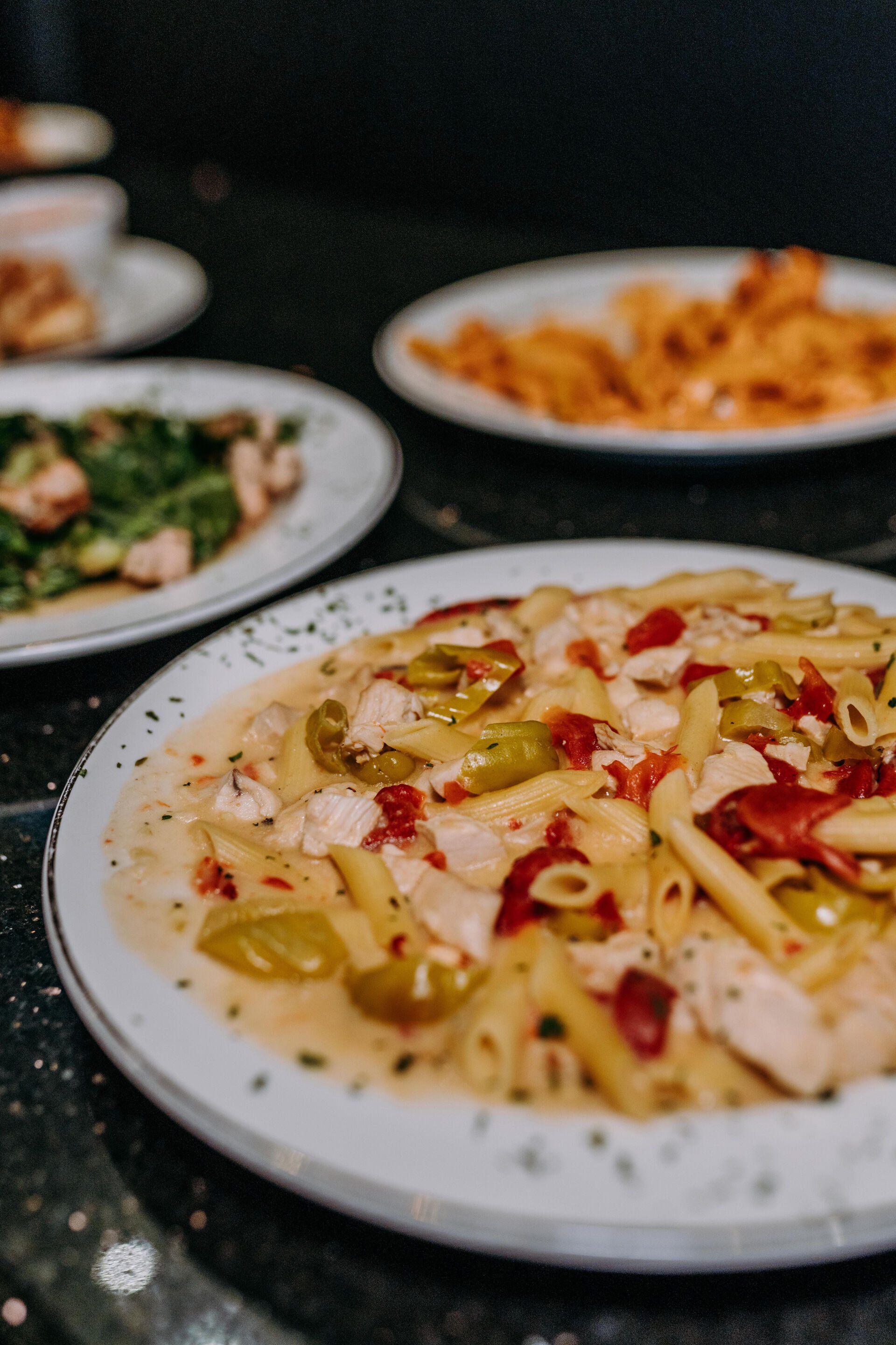 A close up of a plate of pasta with chicken and peppers on a table.