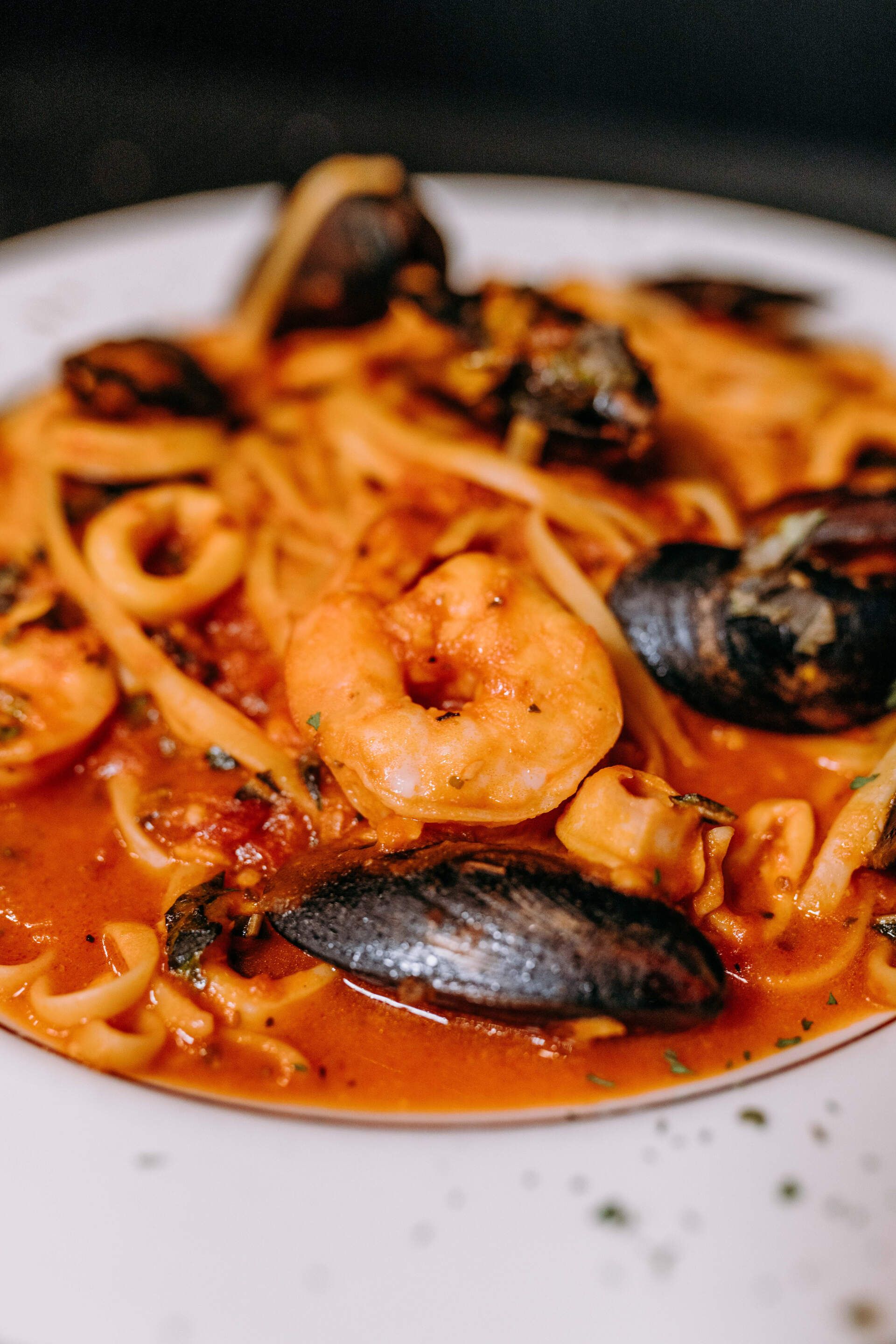 A white plate topped with noodles , shrimp , mussels and sauce.