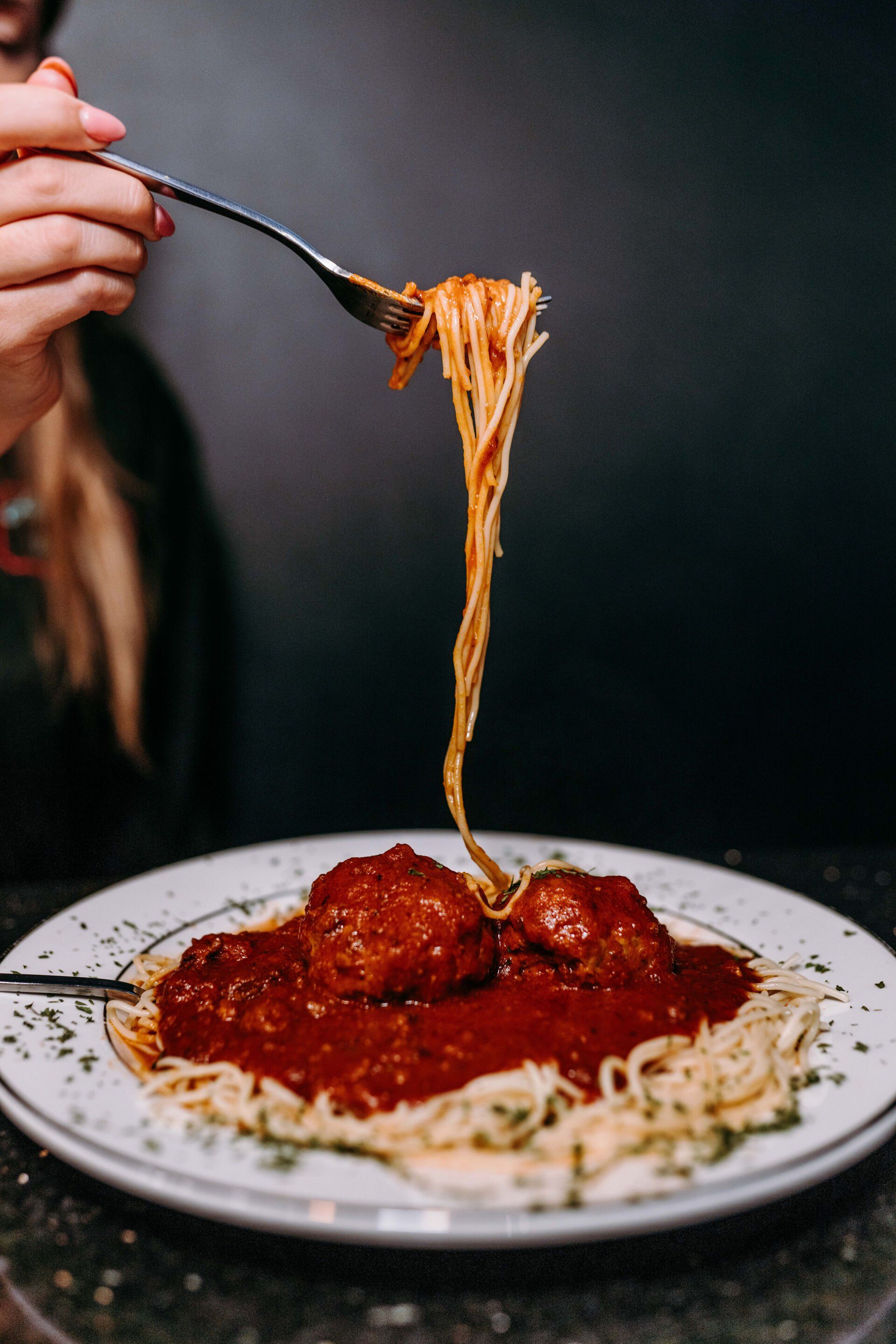 A person is eating spaghetti and meatballs with a fork.