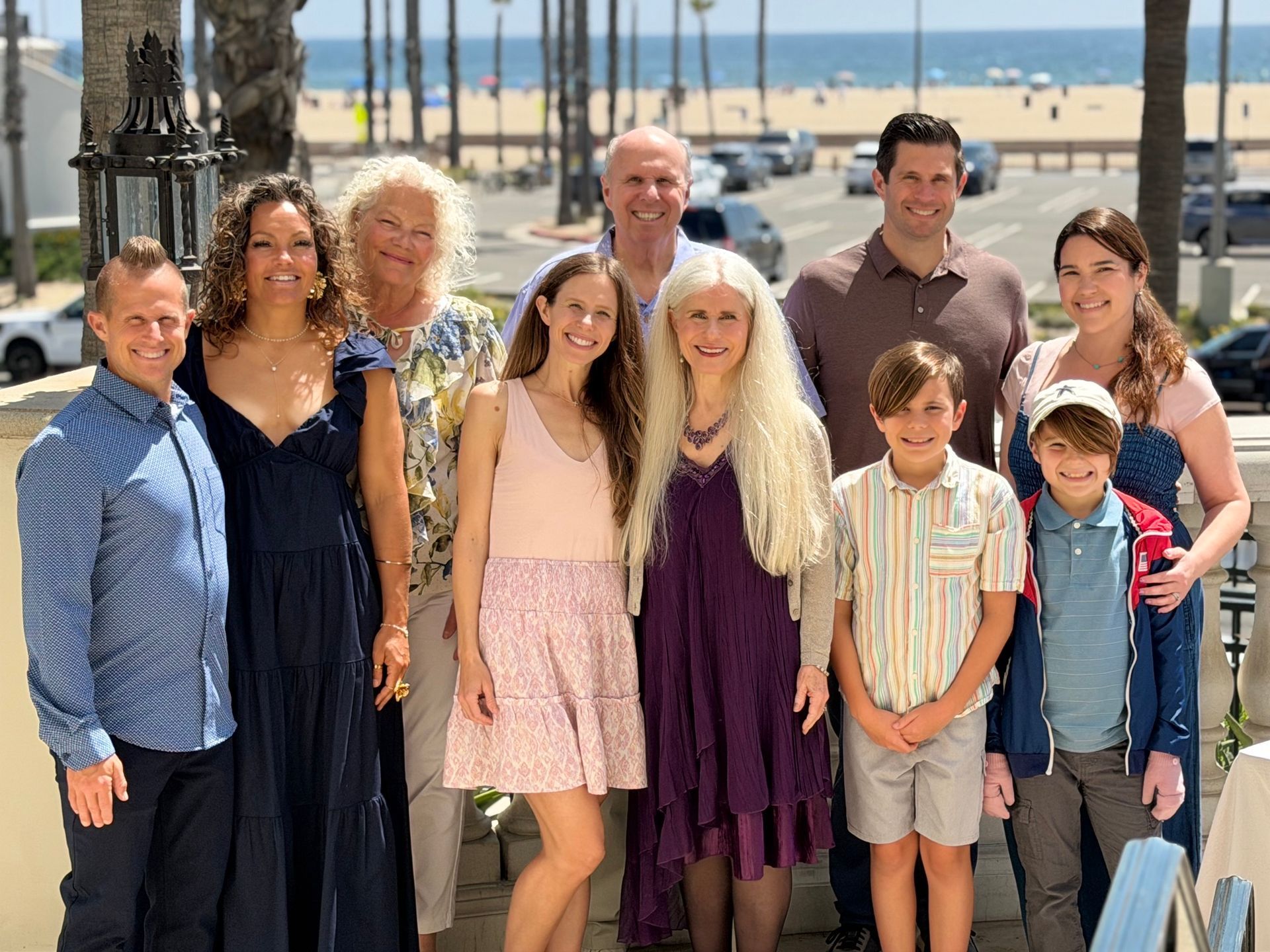 Large family posing on a sunny beach boardwalk with palm trees and a marina in the background