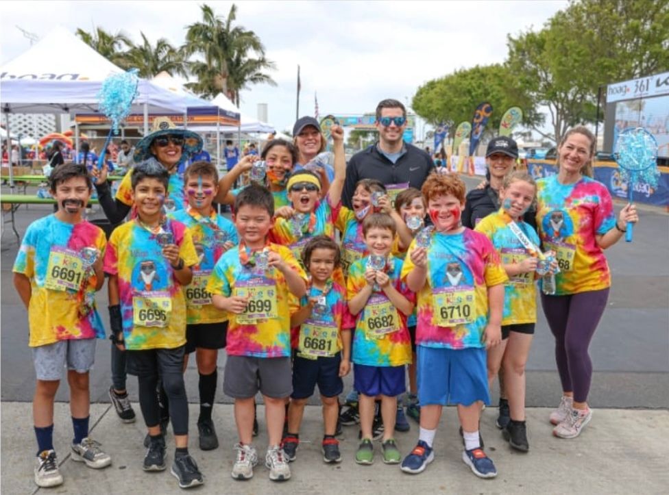 Group of colorful runners posing outdoors before a race, holding medals and smiling at the camera.