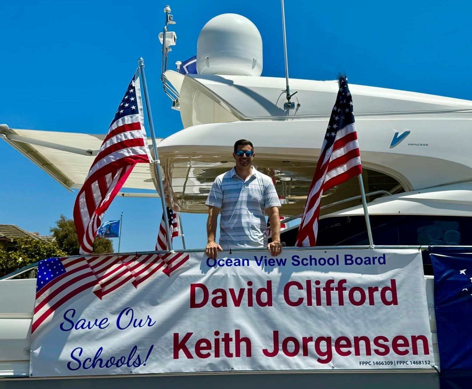 Man standing on a bannered boat with U.S. flags and a sign reading “Save Our Schools” and “David Clifford Keith Jorgensen.”