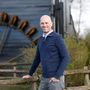 Een man in een blauwe trui leunt op een houten hek.