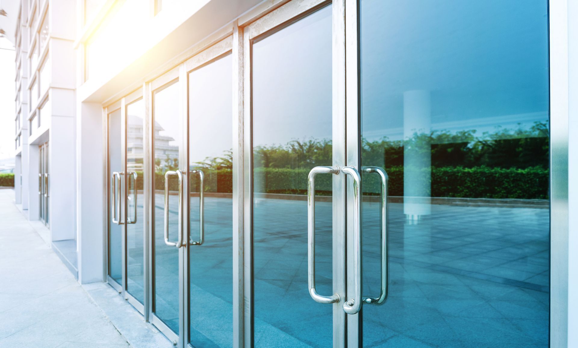 Portes en verre avec poignées argentées sur l'extérieur d'un bâtiment, reflétant le ciel et la verdure environnante.