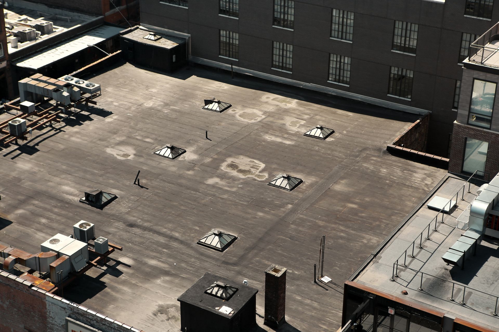 Rooftop with mechanical equipment, vents, and a few small figures walking. Brick and gray buildings.