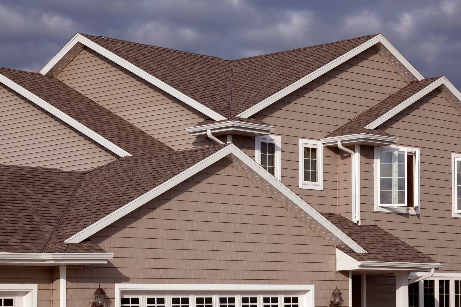 Tan house with brown roof and white trim against a cloudy sky.