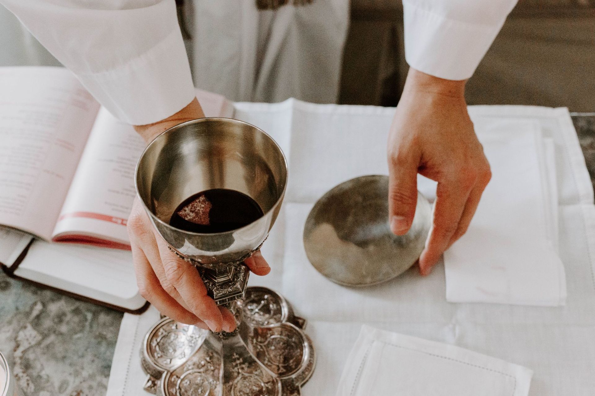Hands arranging metal ritual bowls and a tray on a white cloth altar