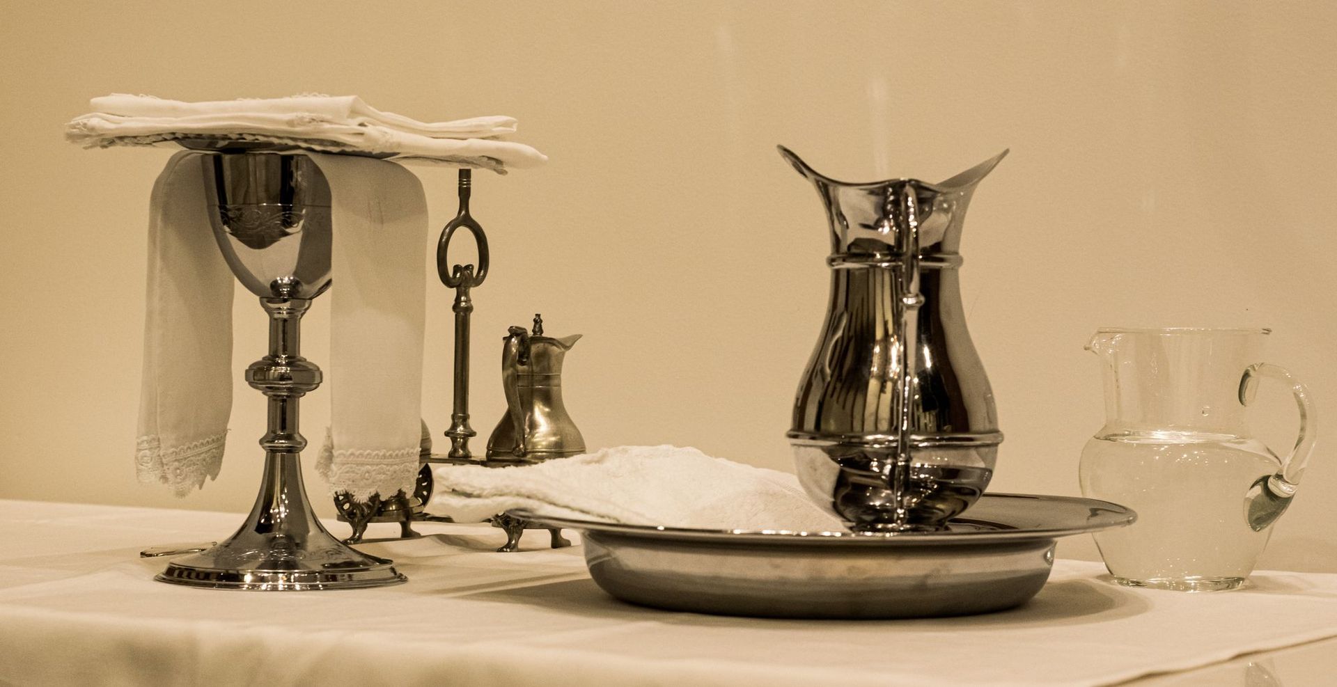 Elegant tea service on a white tablecloth with a silver teapot, cups, saucers, and glassware.